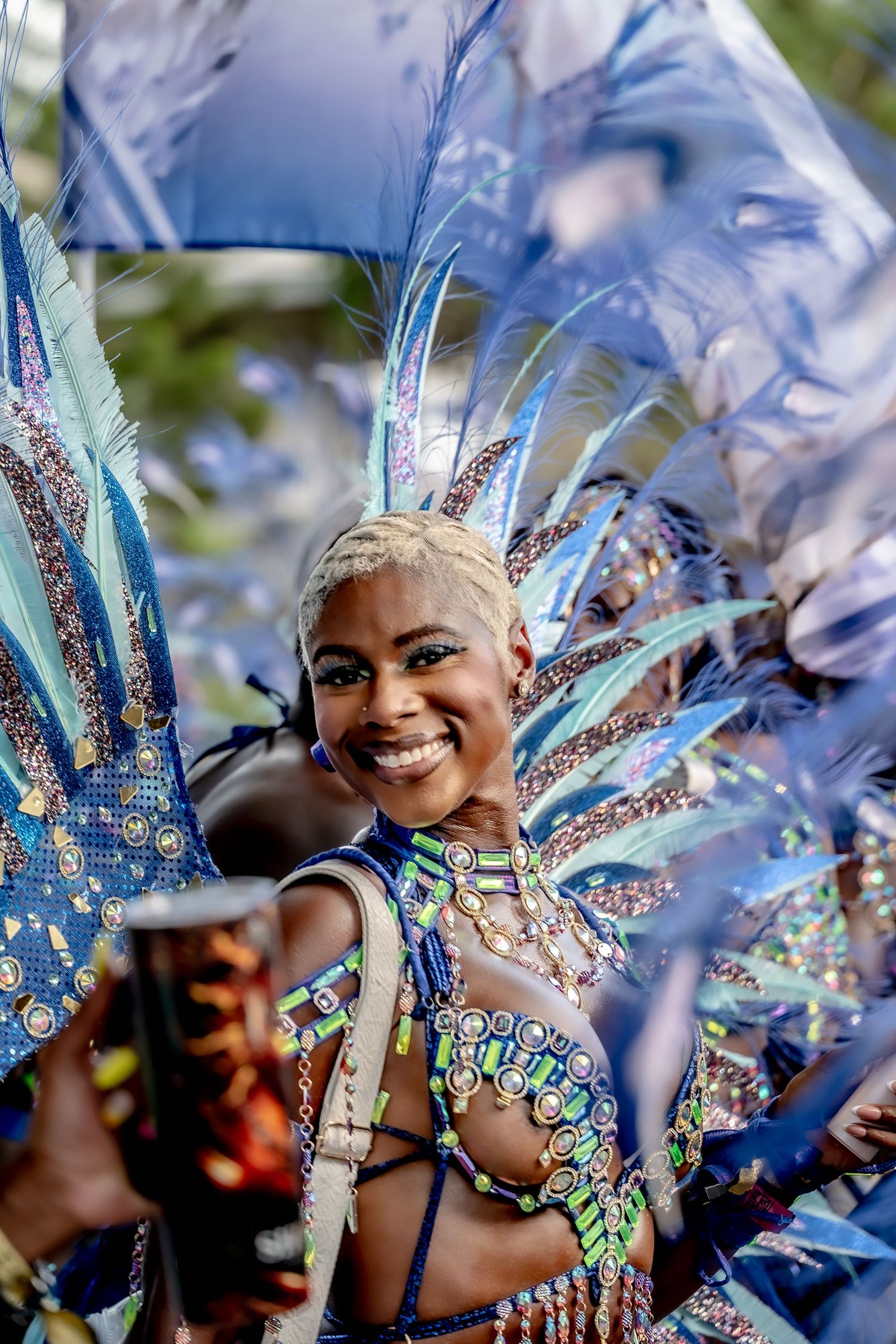 Smiling woman in vibrant blue feathered carnival costume with sequined bodice at a festive parade celebration.