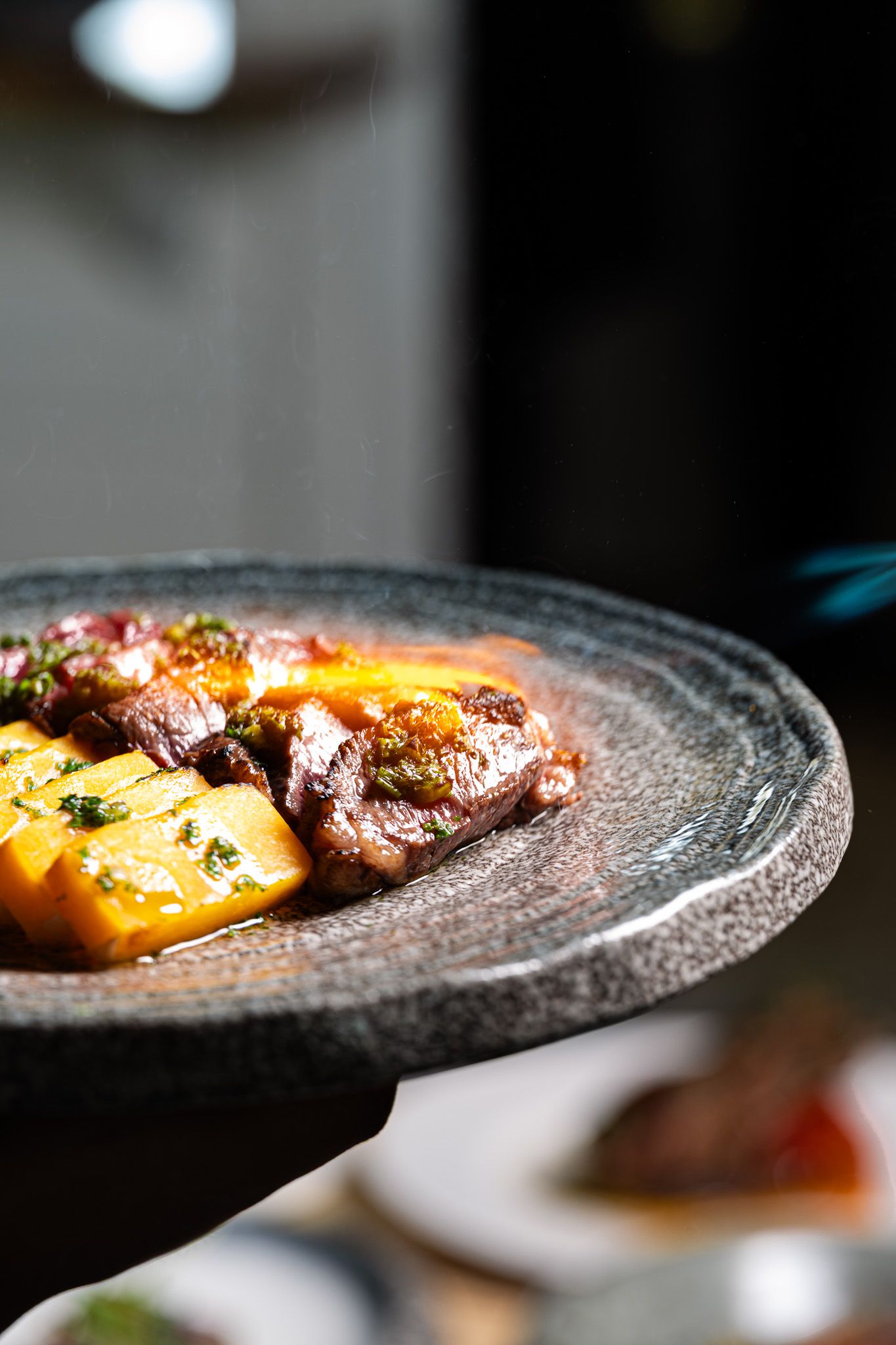 Grilled meat and pineapple chunks served on a rustic stone plate, garnished with fresh herbs in a restaurant setting.