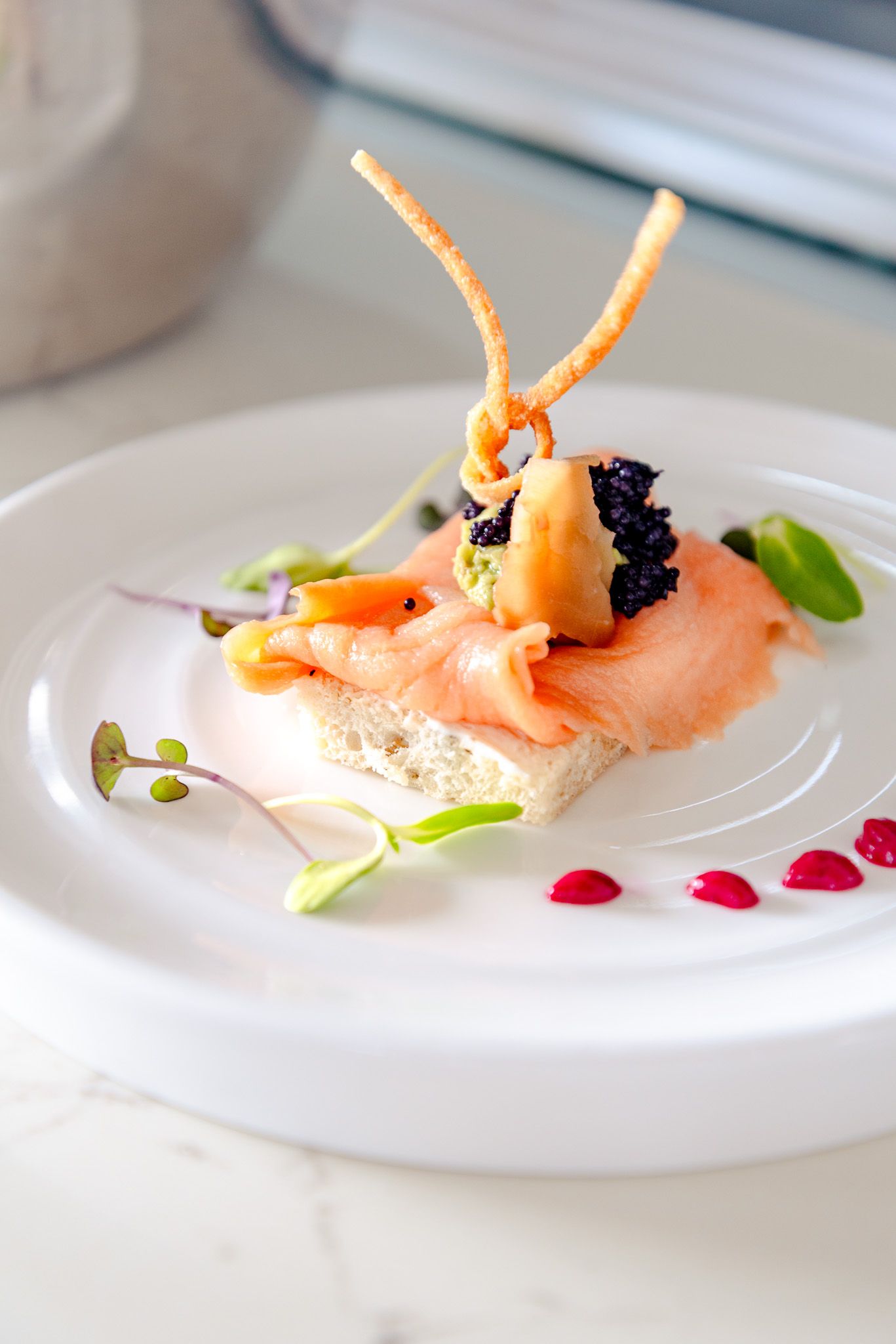 Elegant plated shrimp appetizer with caviar and microgreens on white dish with red sauce dots.
