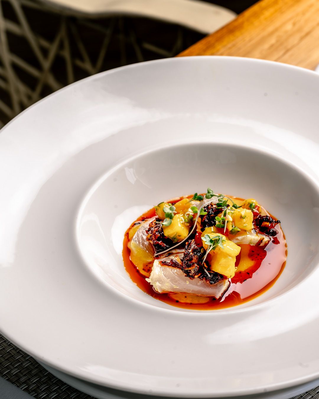 Elegant fine dining dish featuring seared fish with tropical fruit salsa, microgreens, and rich red sauce on a white plate.