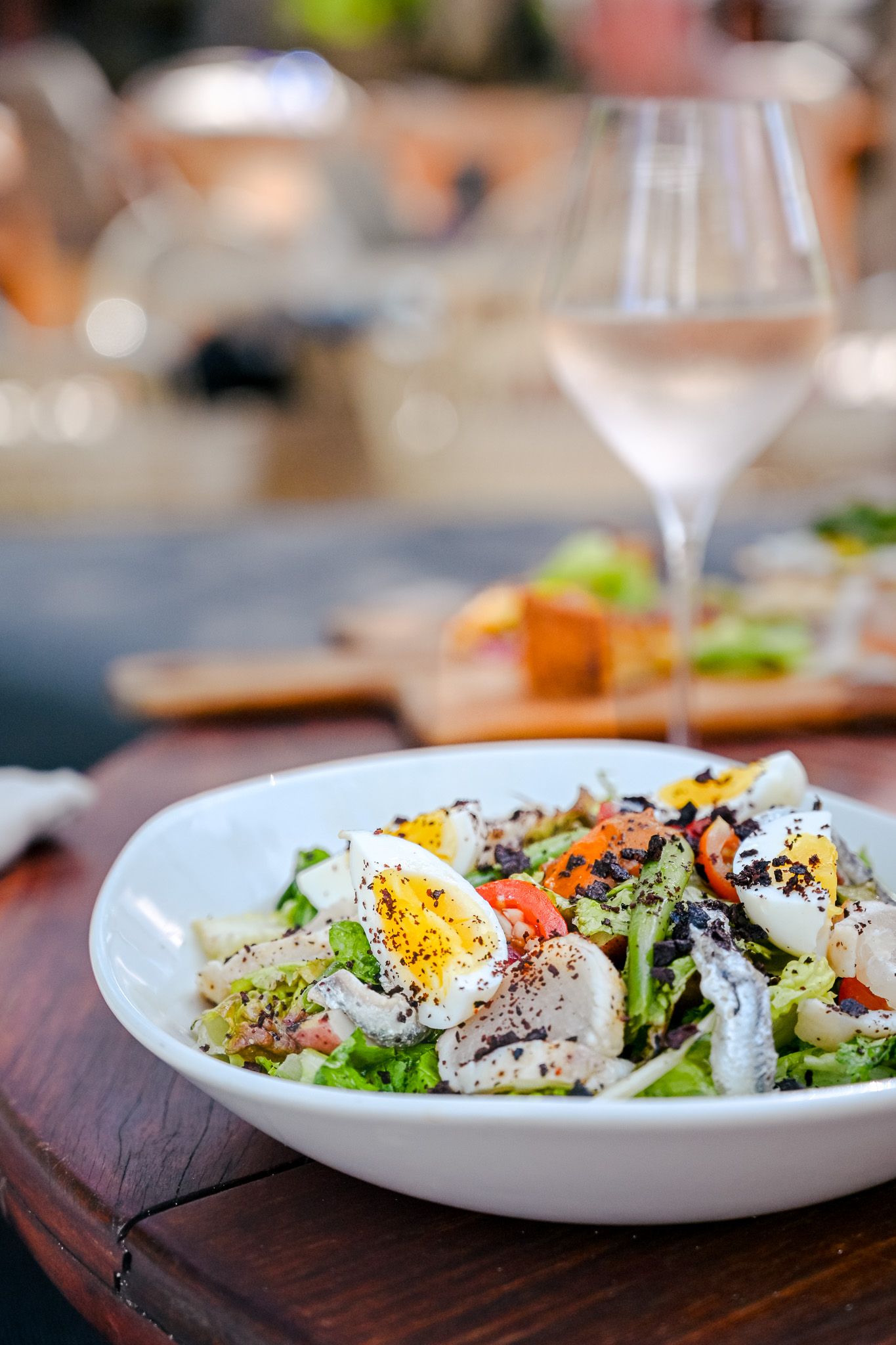 Fresh garden salad with boiled eggs, greens, and black pepper in a white bowl, served with rosé wine.