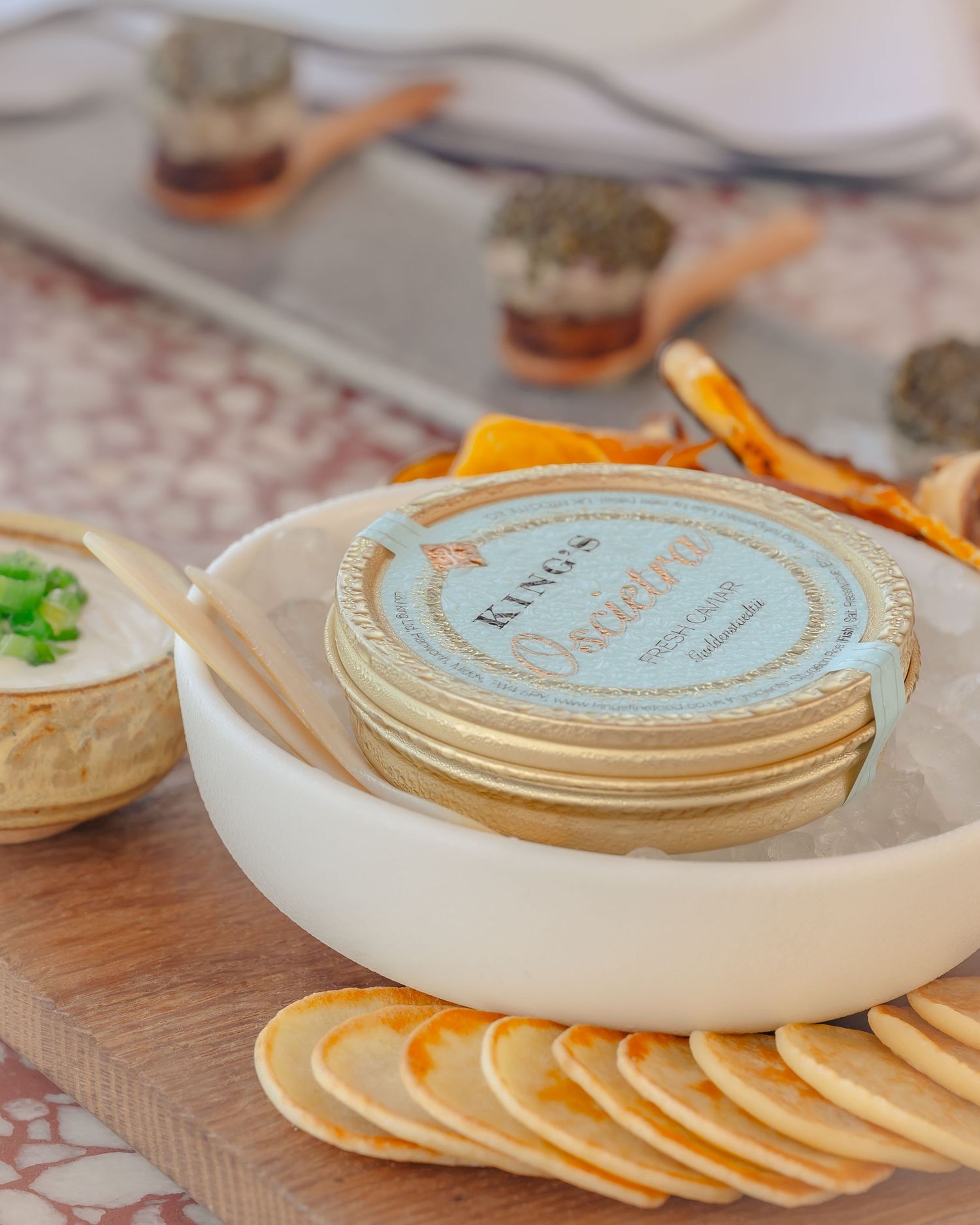 Kings Caviar tin displayed on a white plate with crackers, dip, and garnishes on a wooden board.