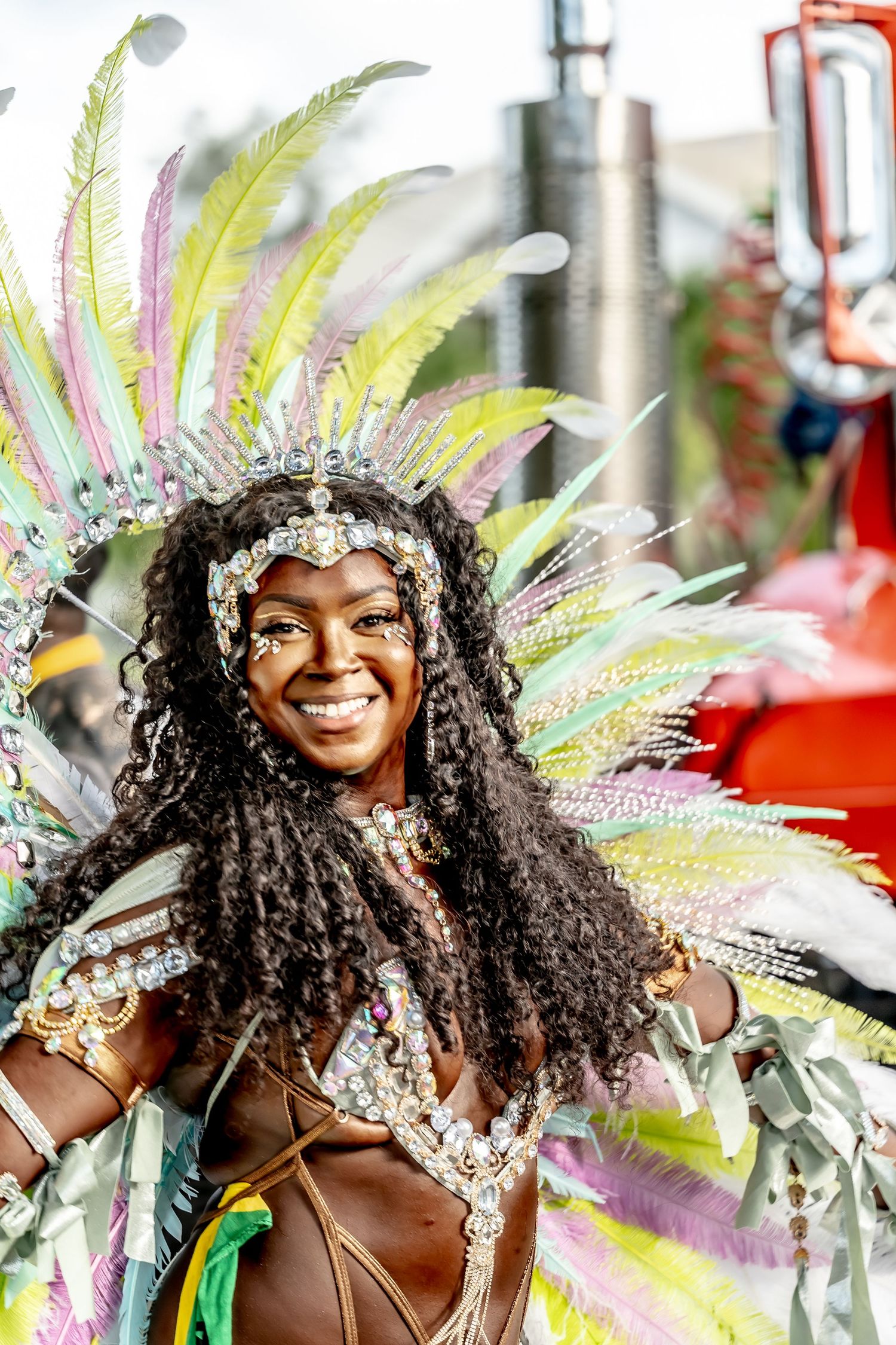 Smiling woman in vibrant carnival costume with colorful feathers, sequins, and headdress at a festive parade celebration.