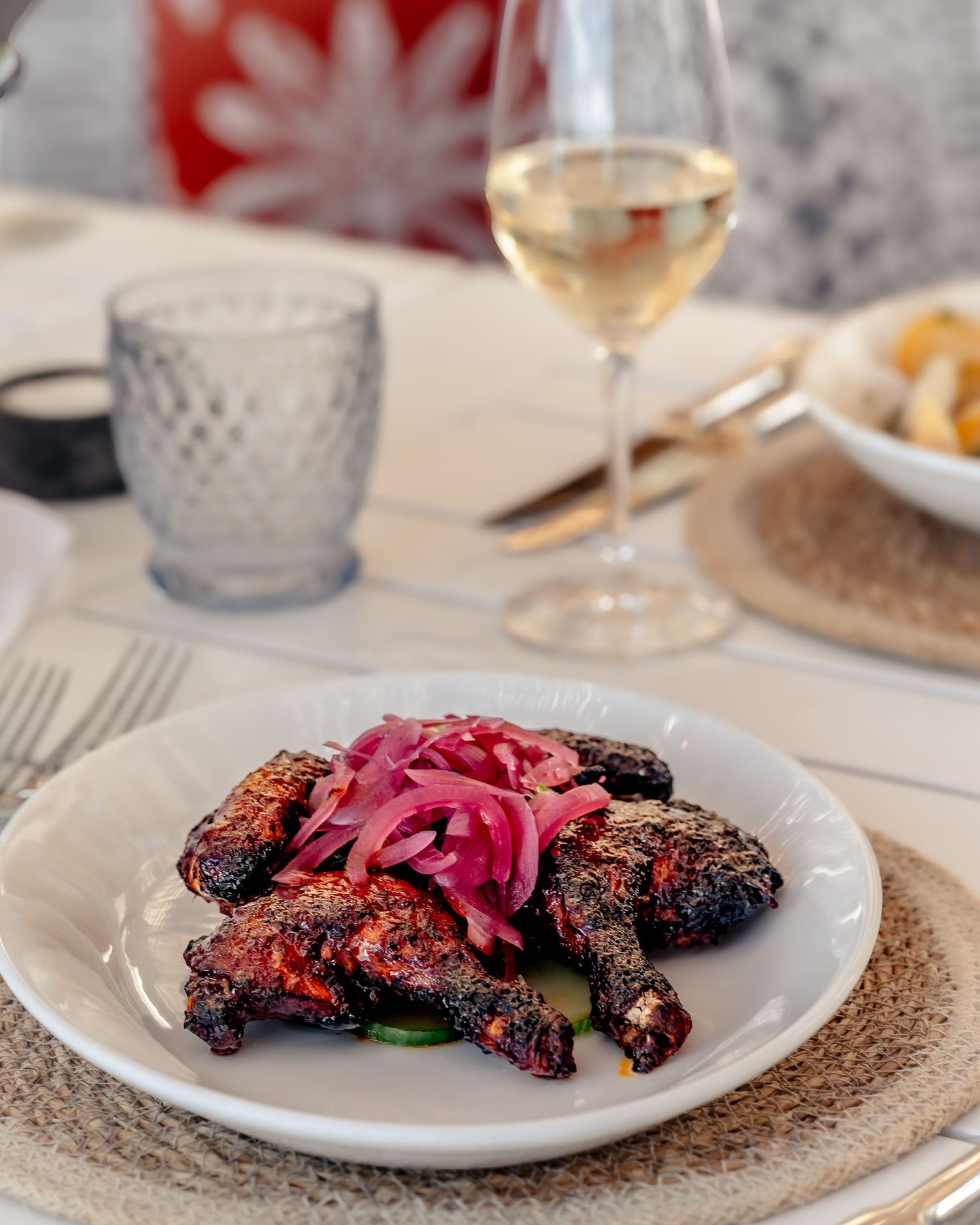 Grilled spiced chicken with pickled red onions on a white plate, served with white wine at an elegant restaurant table.