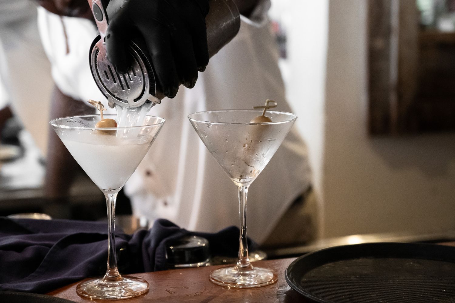 Red wine being poured into elegant wine glasses in a dimly lit restaurant setting.