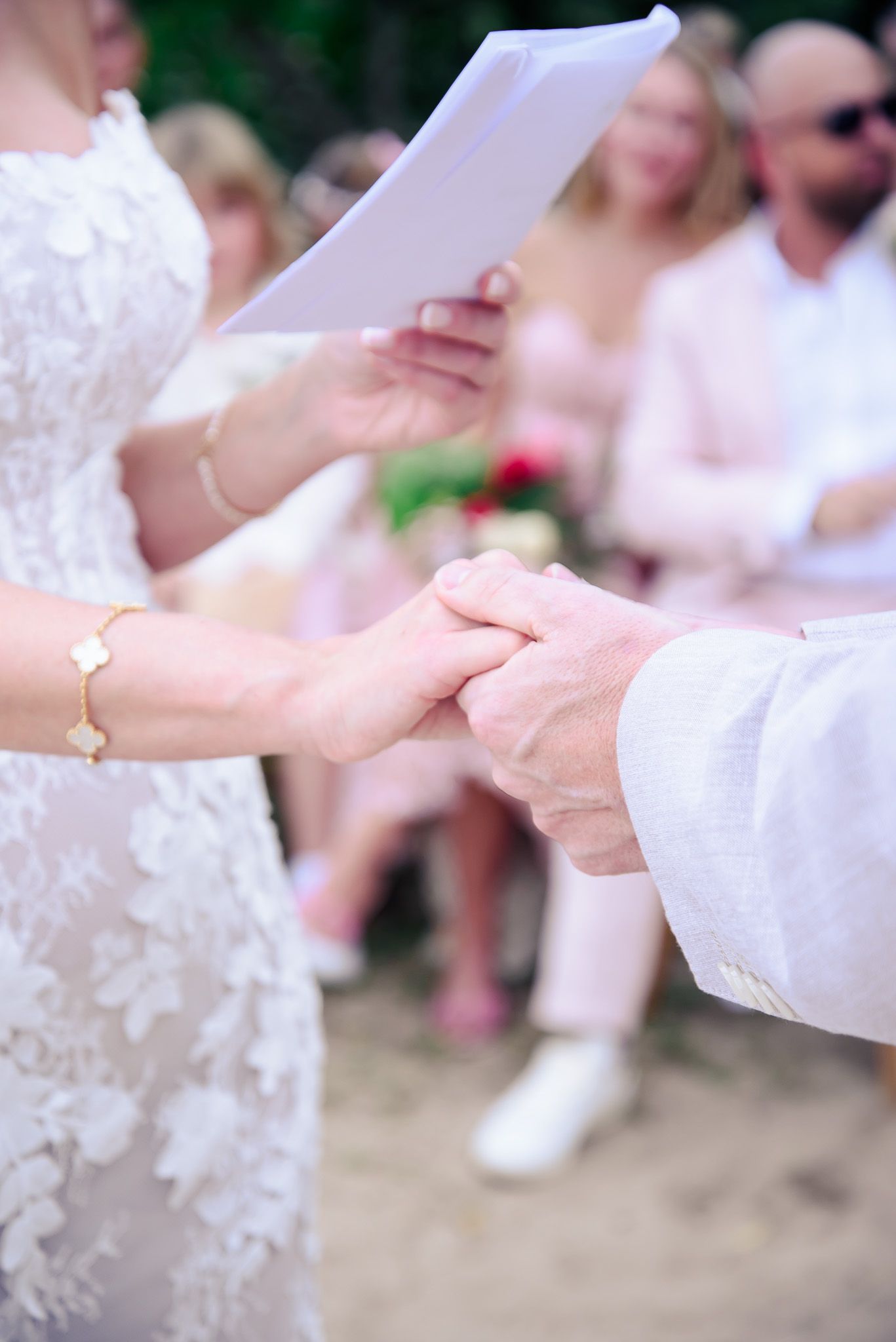 Close-up of hands exchanging rings during an outdoor wedding ceremony with guests in the background.