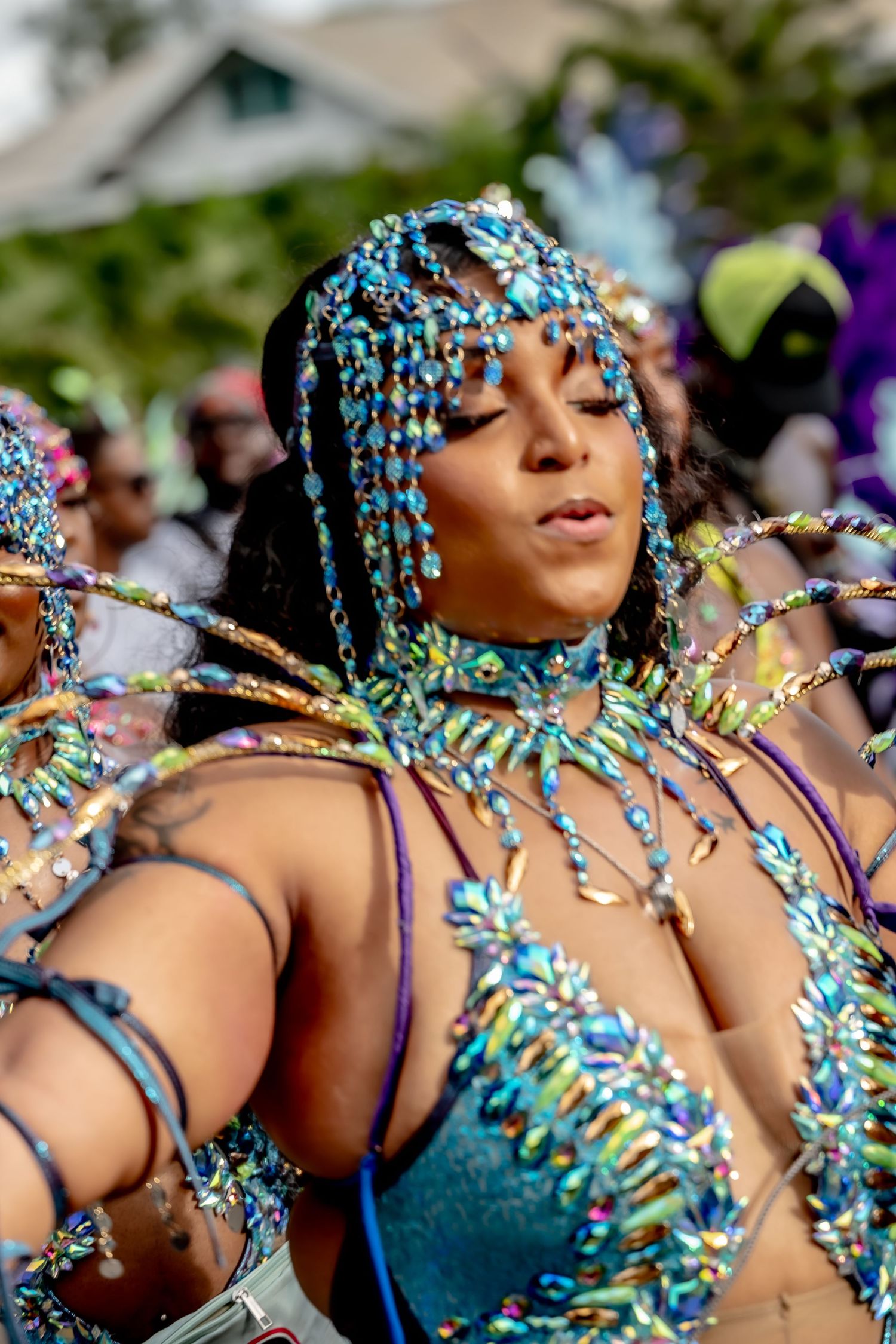 Woman in vibrant turquoise beaded carnival costume with jeweled headdress dancing at a colorful festival parade.