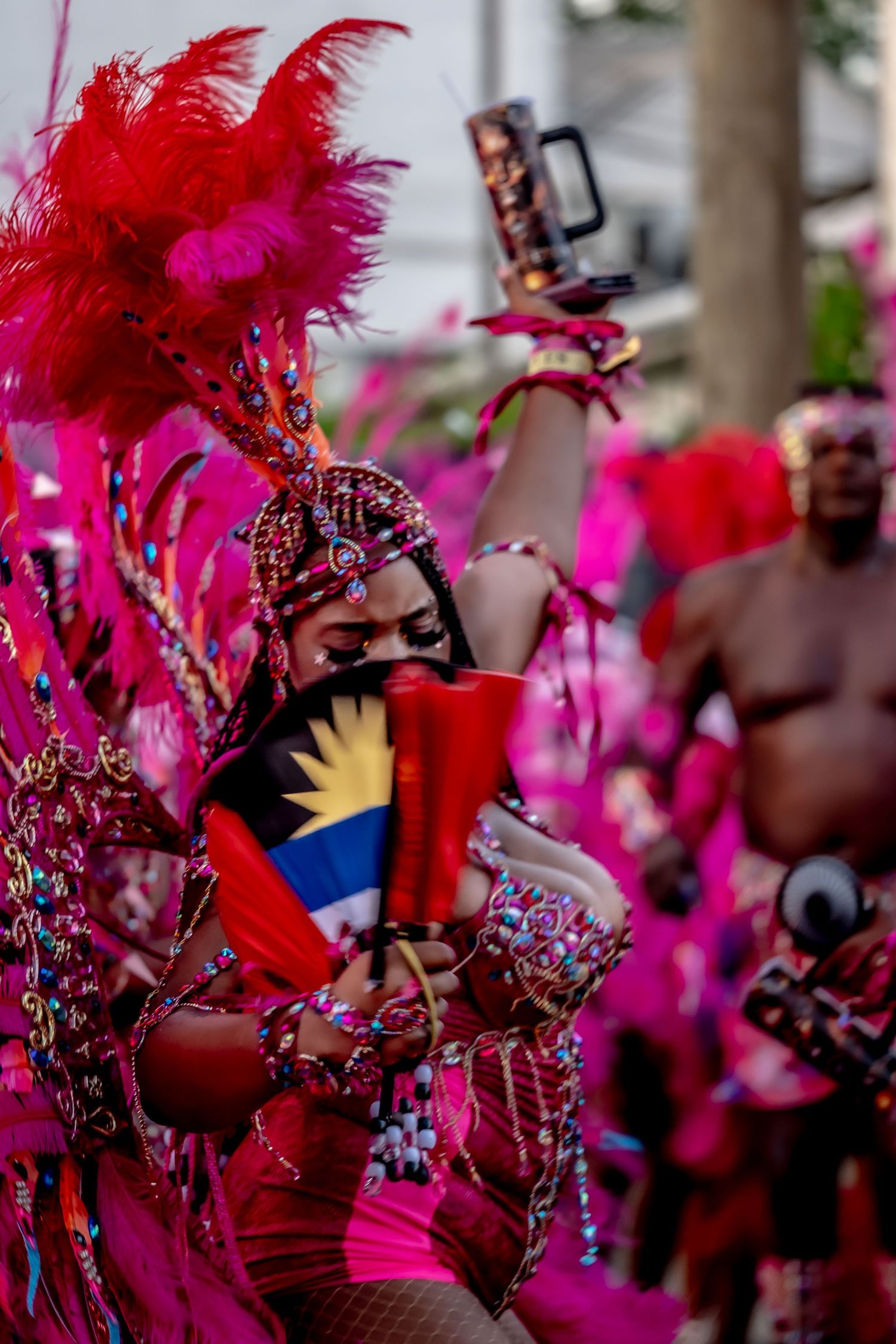 Vibrant carnival dancer in red feathered costume holds Antigua and Barbuda flag during colorful festival parade.