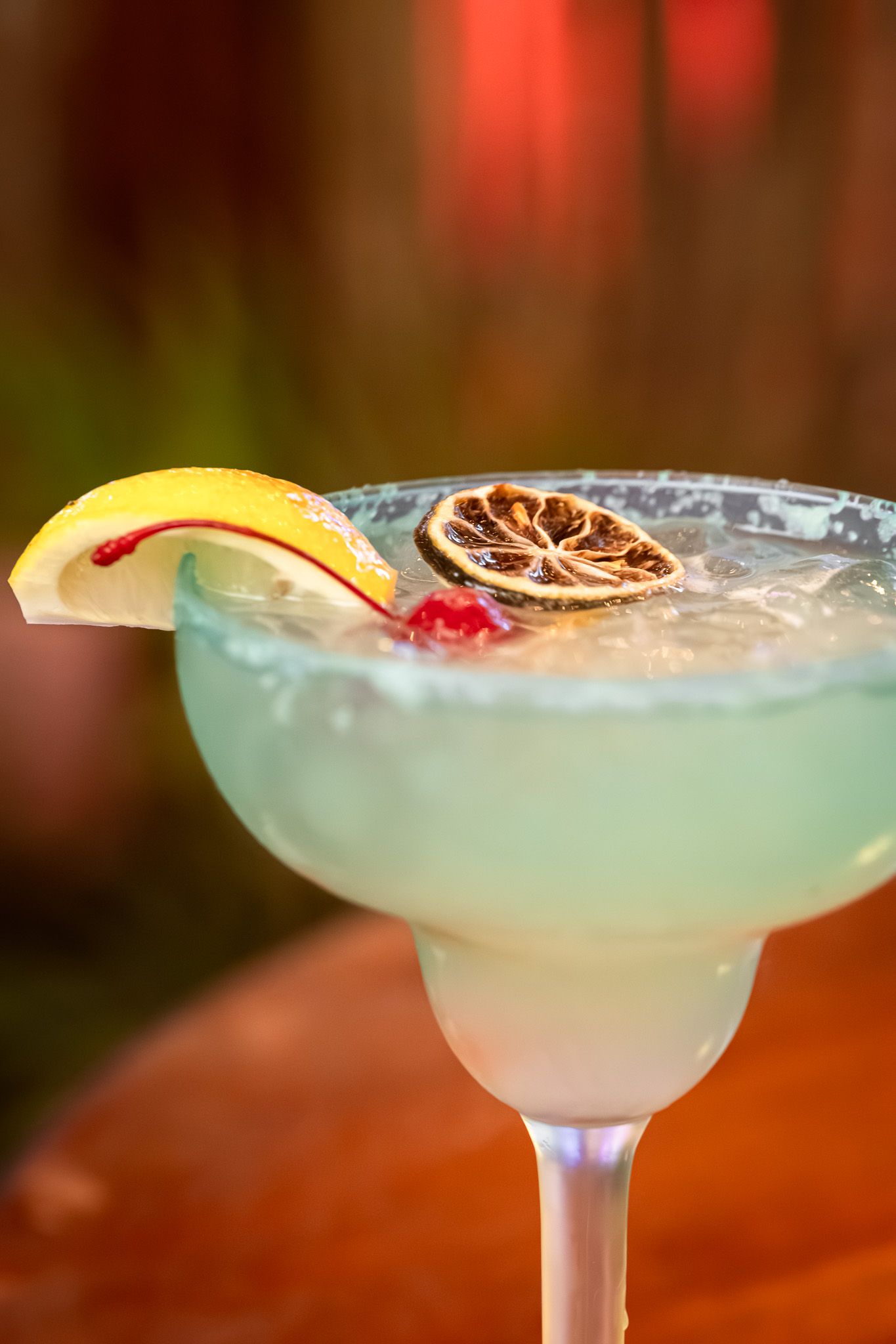 Margarita cocktail garnished with apple slice and dried citrus on rim of glass.
