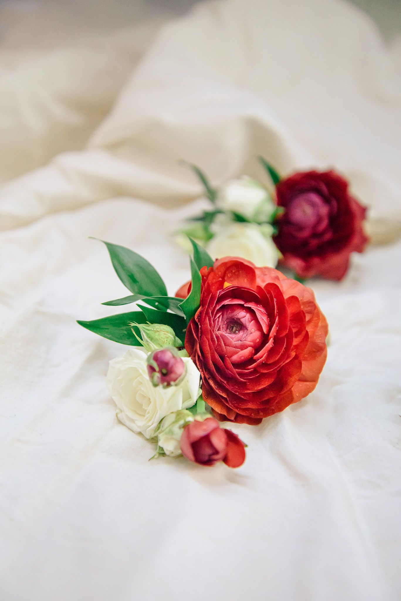 Red and white roses with green leaves arranged artistically on soft white fabric.