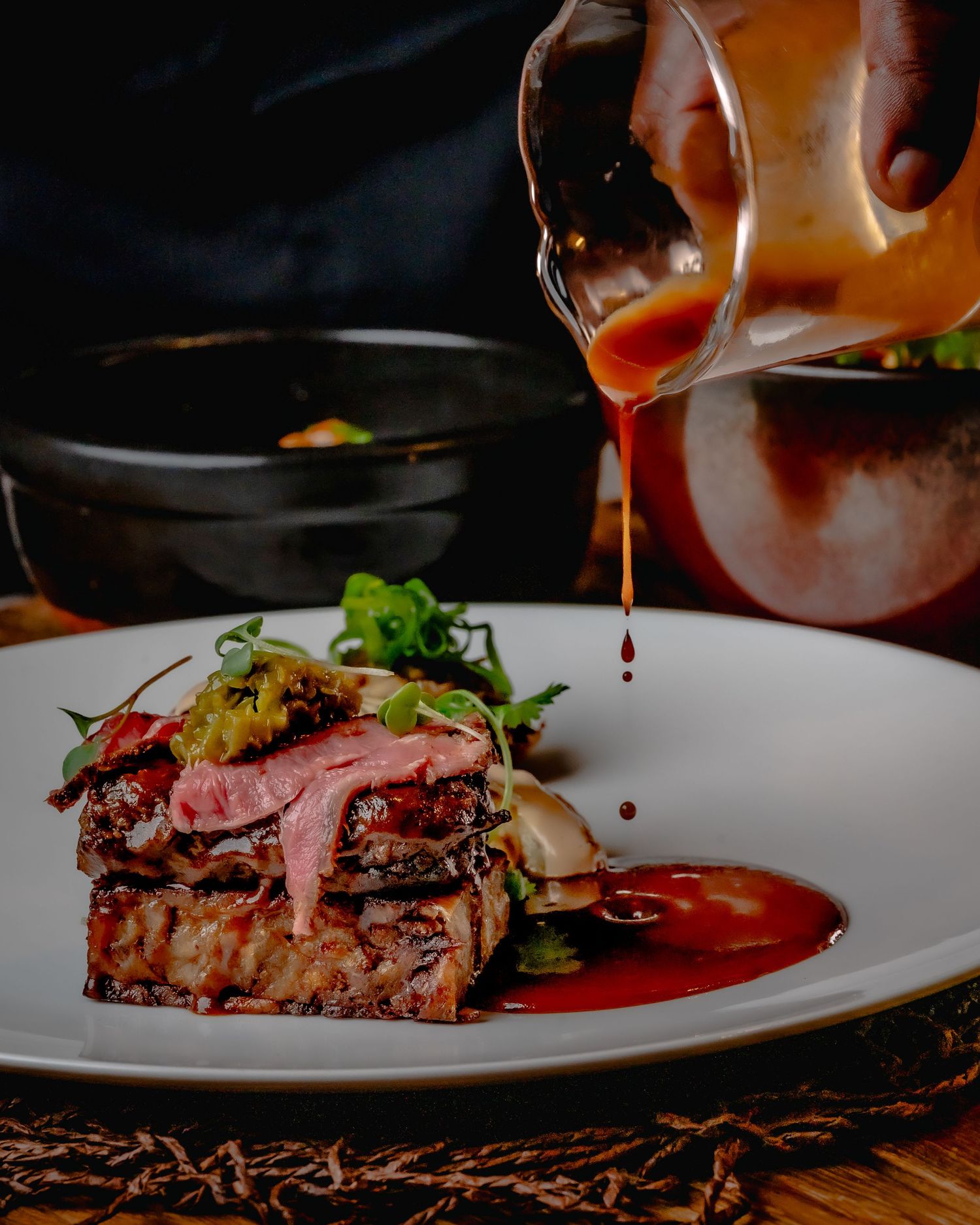 A juicy sliced steak on a white plate being drizzled with rich red sauce in an elegant restaurant setting.