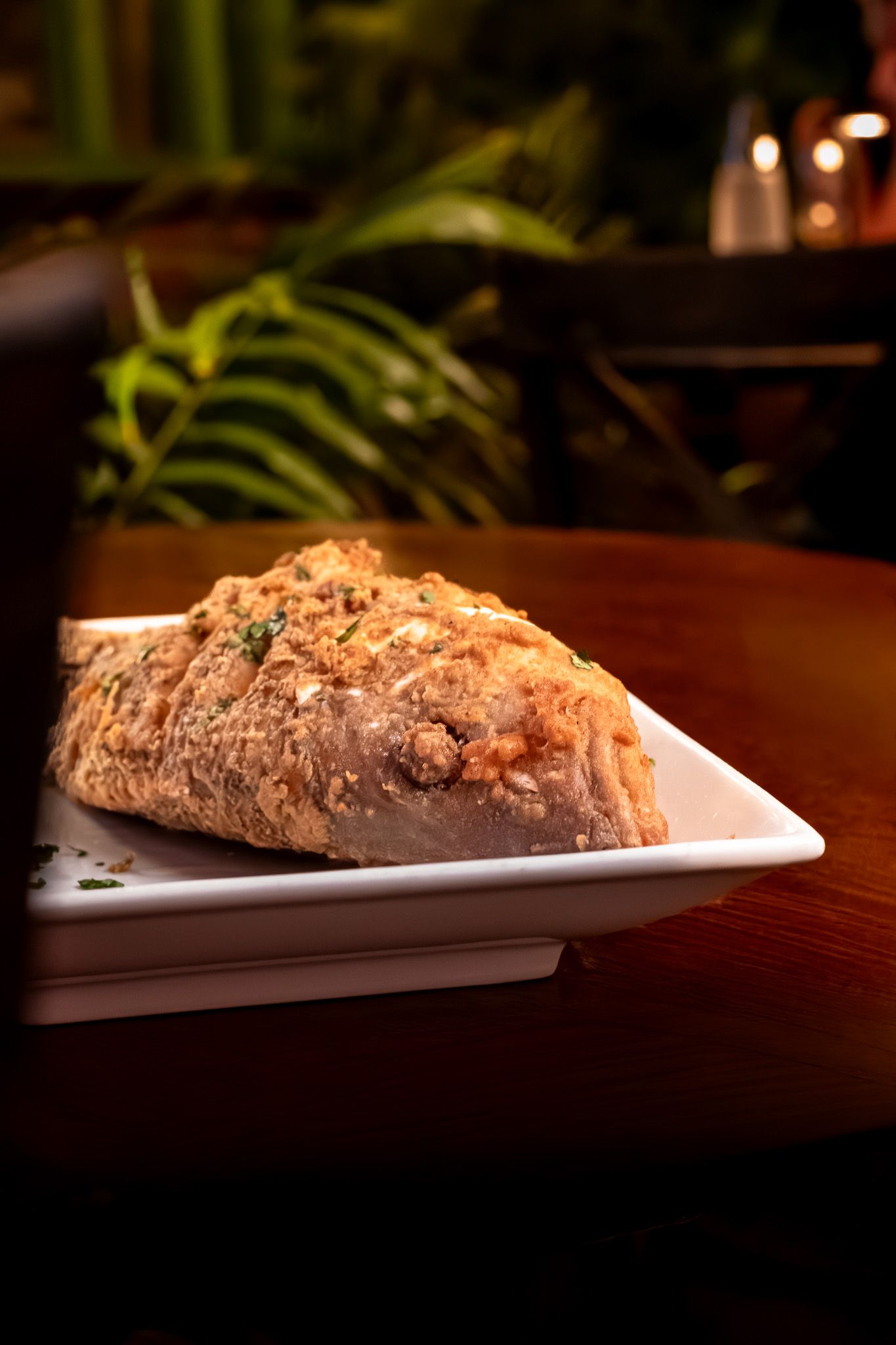 Close-up view of grilled salmon fillet on white rectangular plate in dim restaurant lighting.