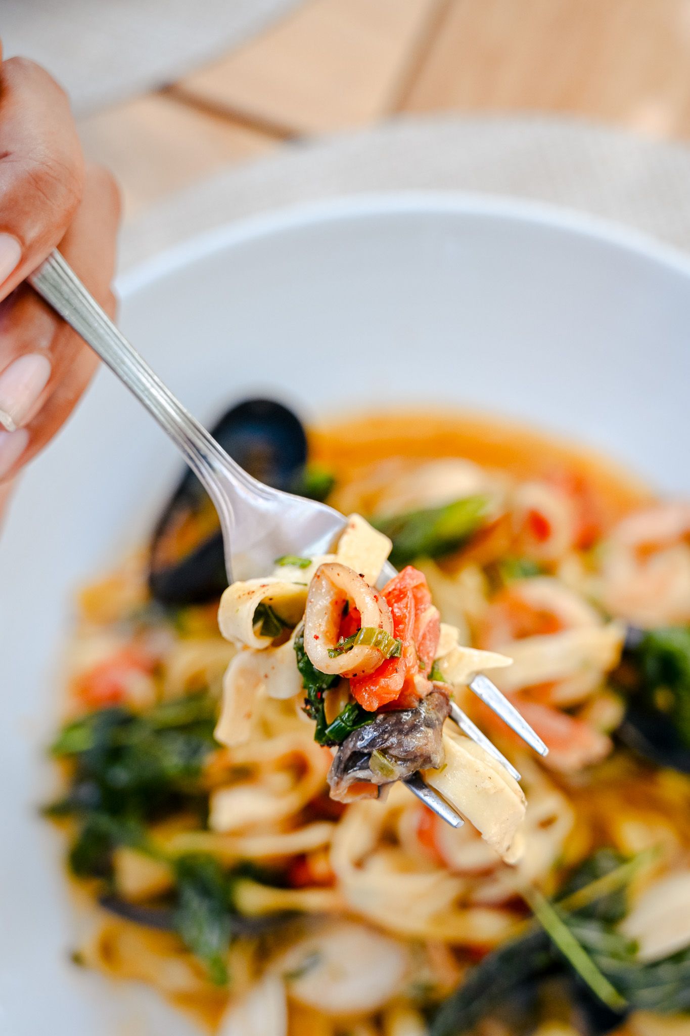 Seafood pasta dish with shrimp and calamari in a light sauce being twirled on a fork.