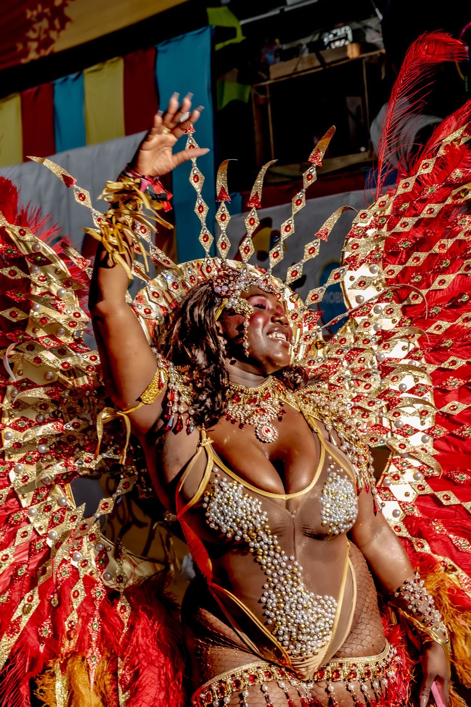 Woman in elaborate red and gold carnival costume with feathered wings performing at a festive celebration.