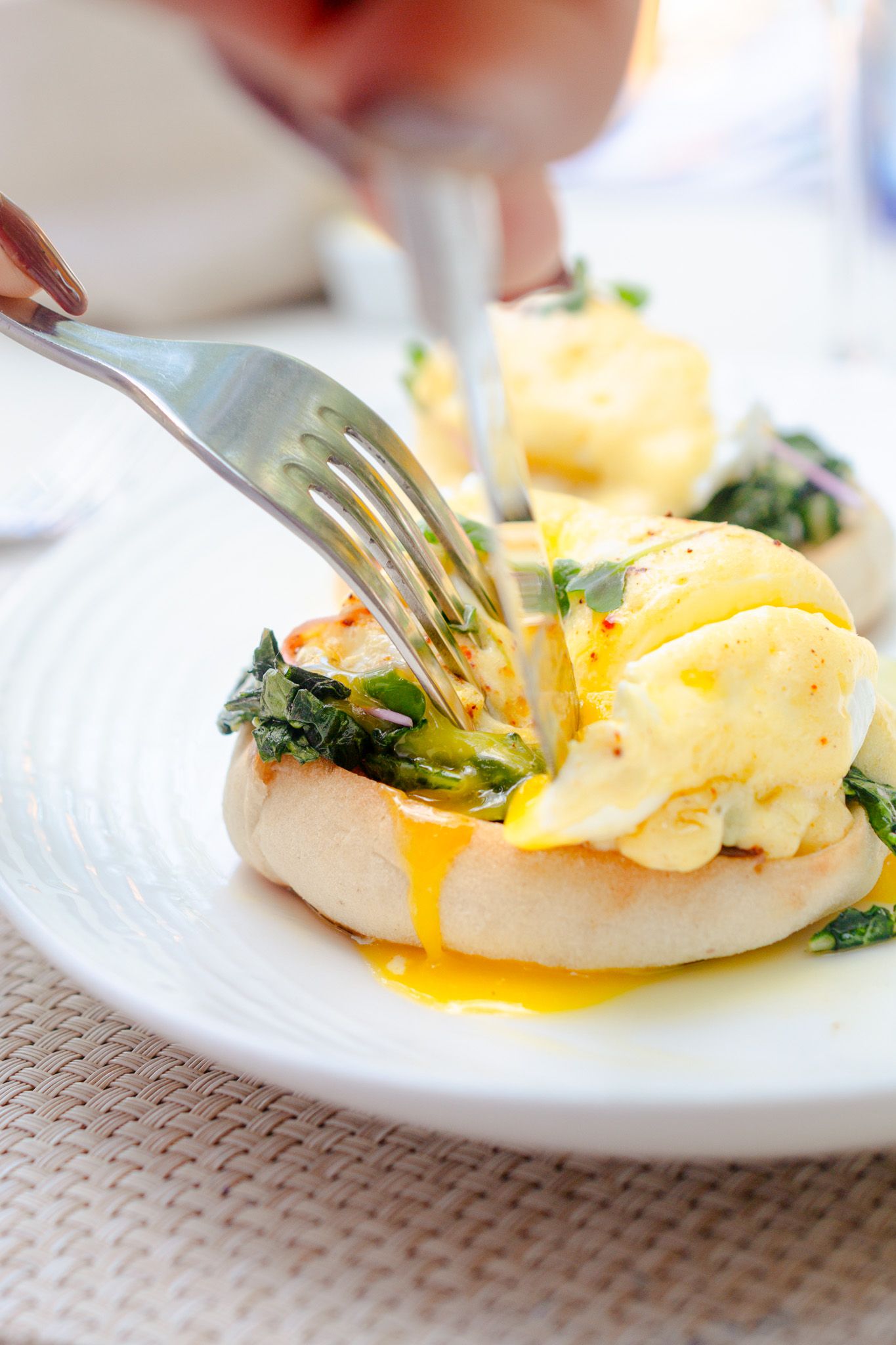 Close-up sequence of eggs Benedict being served showing runny yolk dripping over English muffin with spinach.