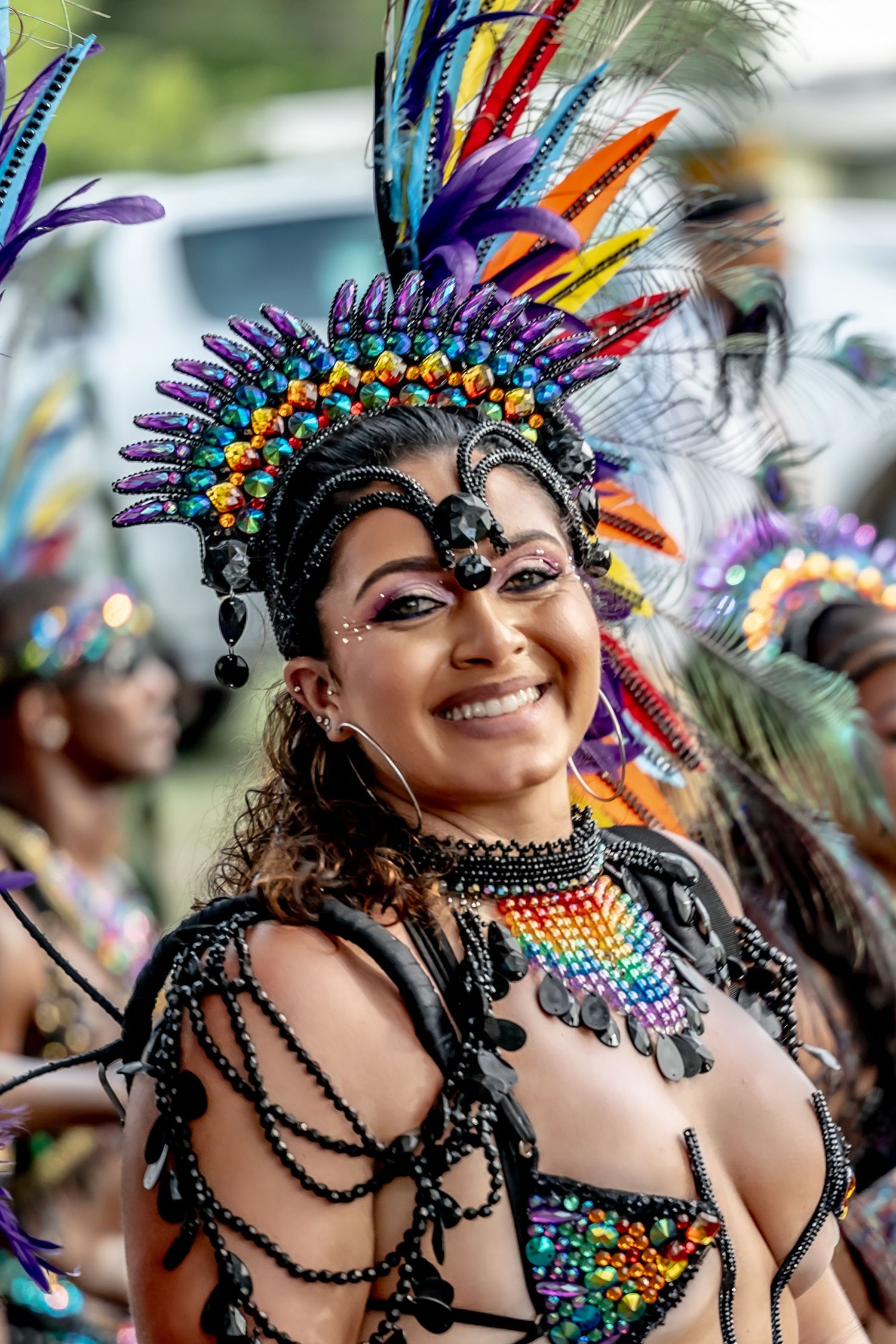 Smiling woman in colorful carnival costume with rainbow feathered headdress and beaded outfit at festive parade.