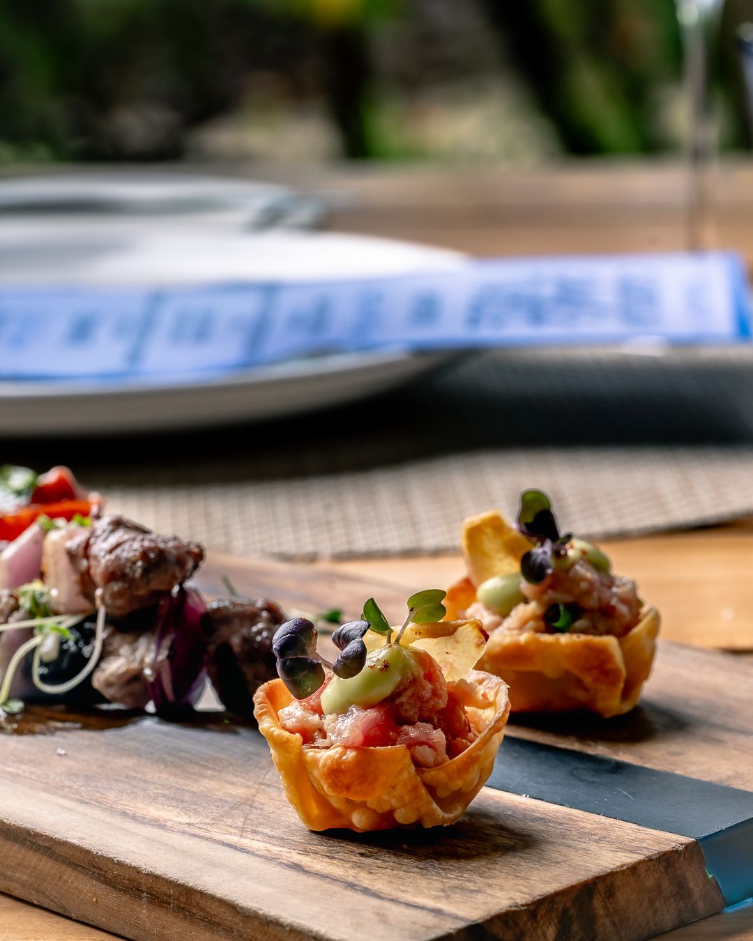 Crispy taco cups filled with fresh salsa and toppings on a wooden board, with meat skewers in the background.