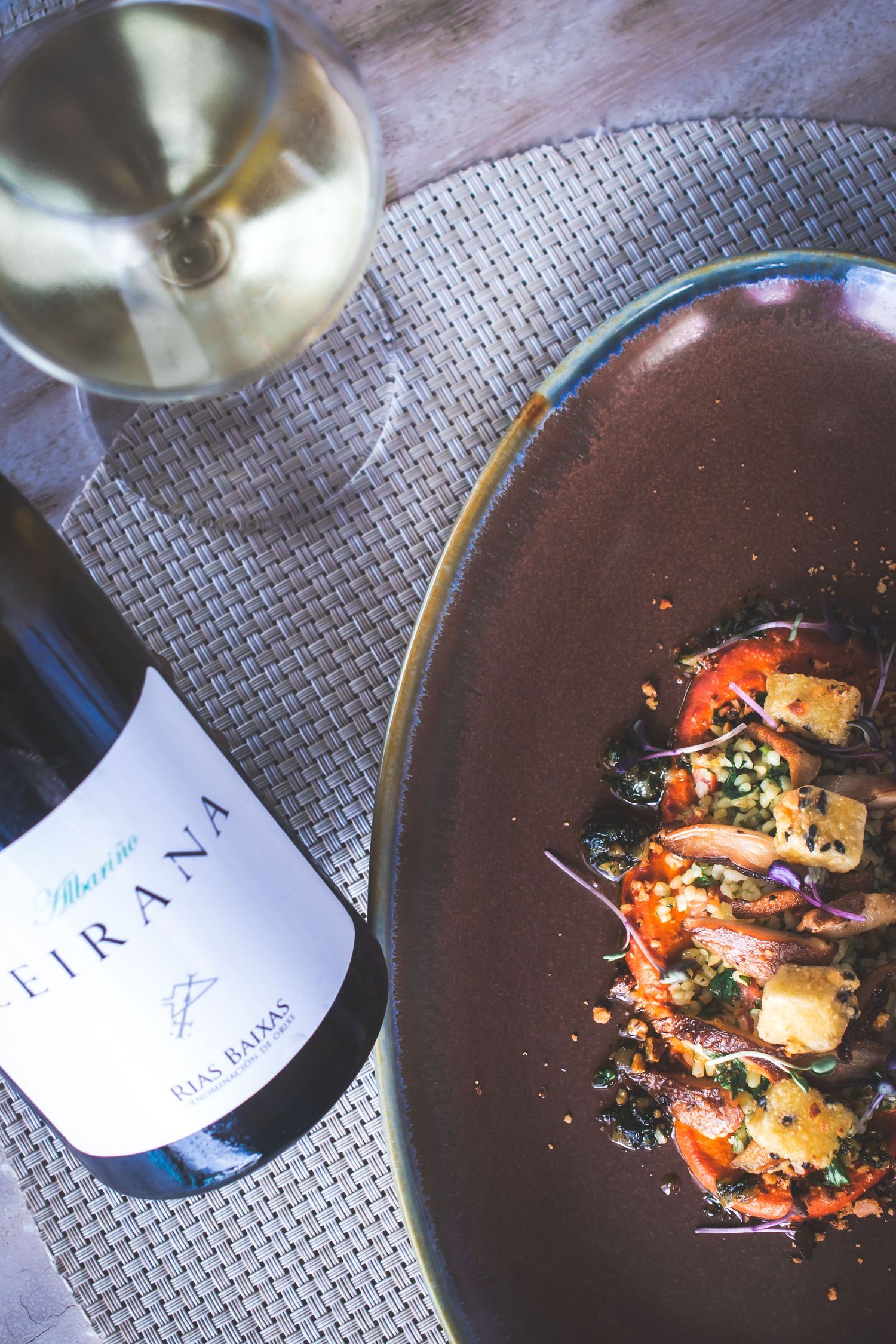 Villanueva Tirana Rias Baixas white wine bottle beside a gourmet seafood dish on a dark ceramic plate.