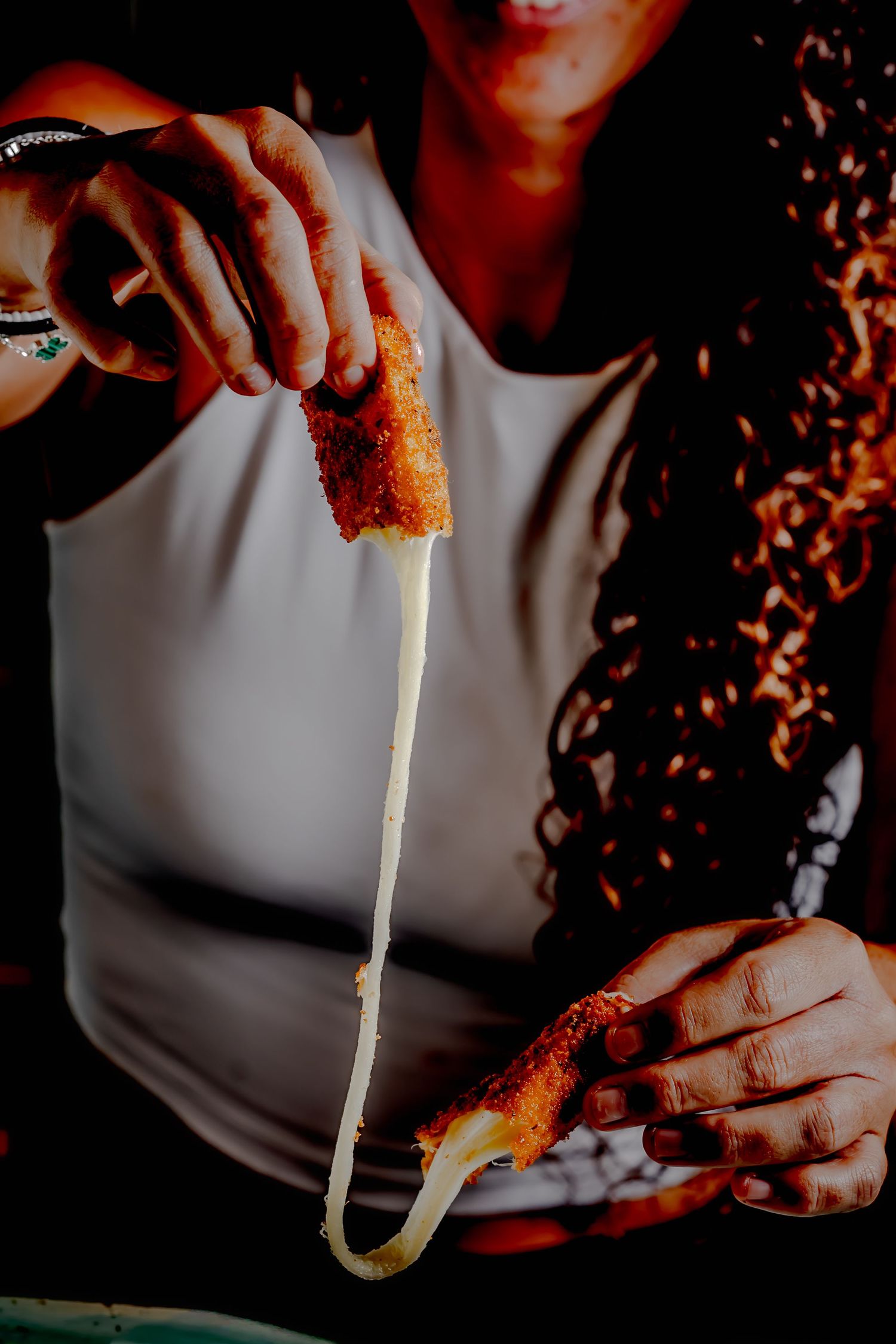 Woman pulling apart a golden fried mozzarella stick with melted cheese stretching between the two pieces.