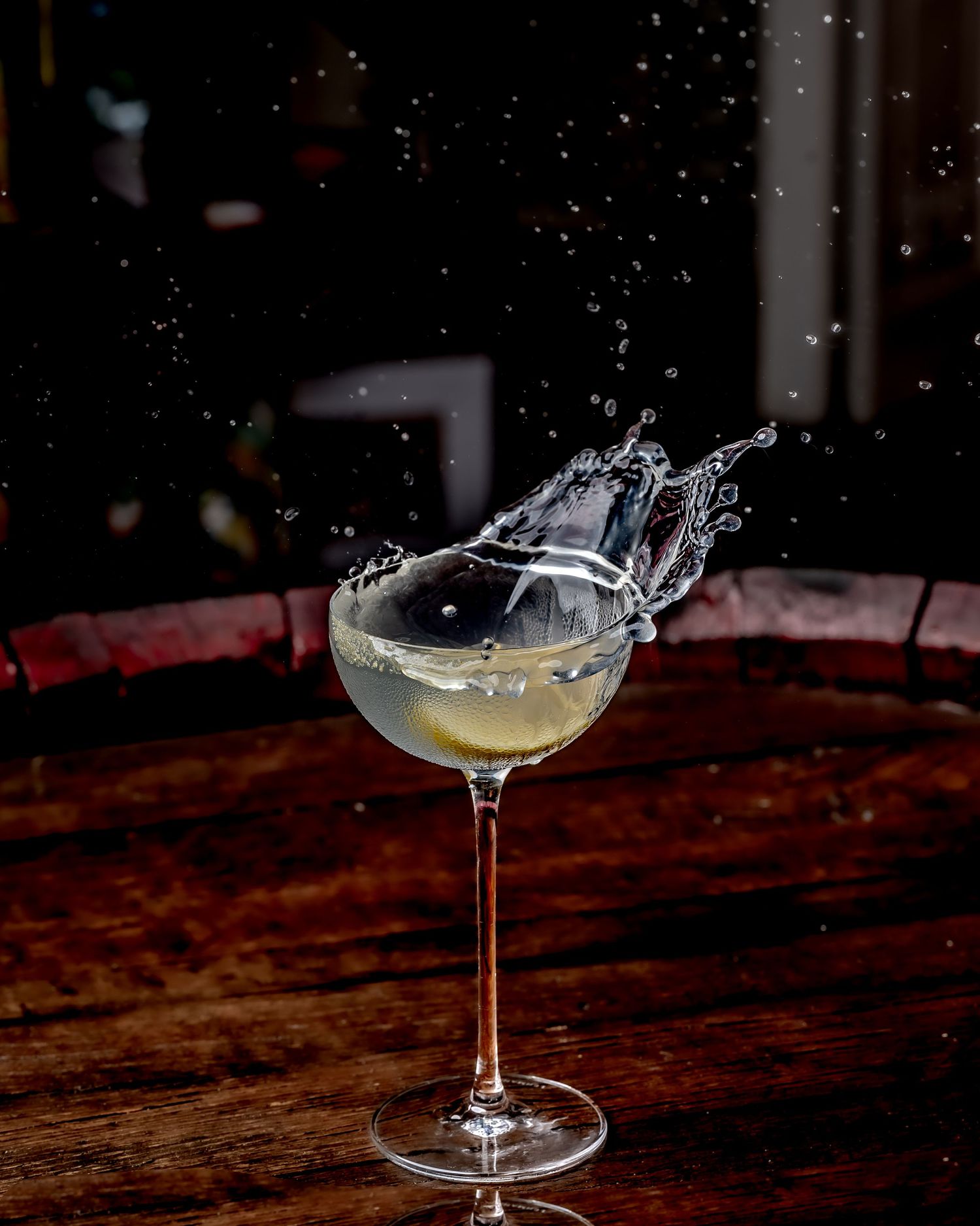 A cocktail in a coupe glass with a dramatic liquid splash on a dark wooden table.