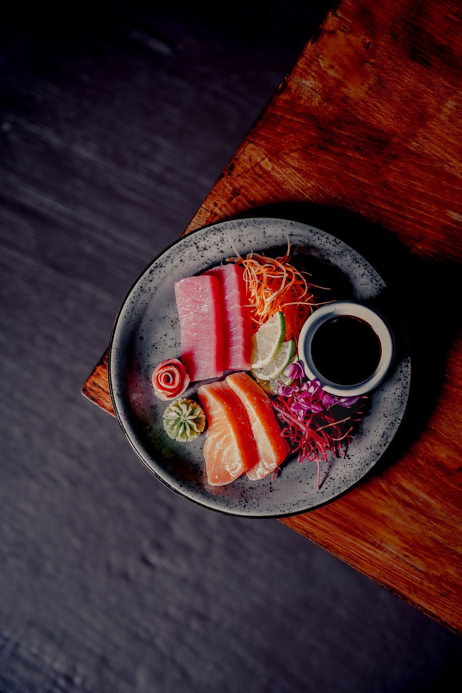 Elegant sashimi platter with tuna, salmon slices, soy sauce, lime, and garnishes on a ceramic plate.