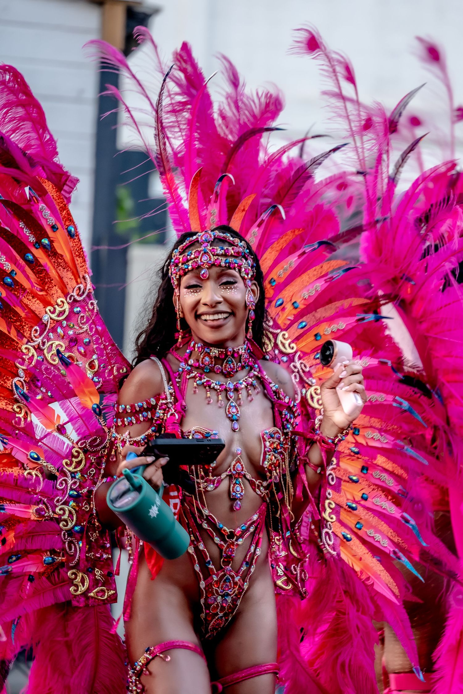 Woman in vibrant pink feathered carnival costume smiling and dancing at a festive parade celebration.