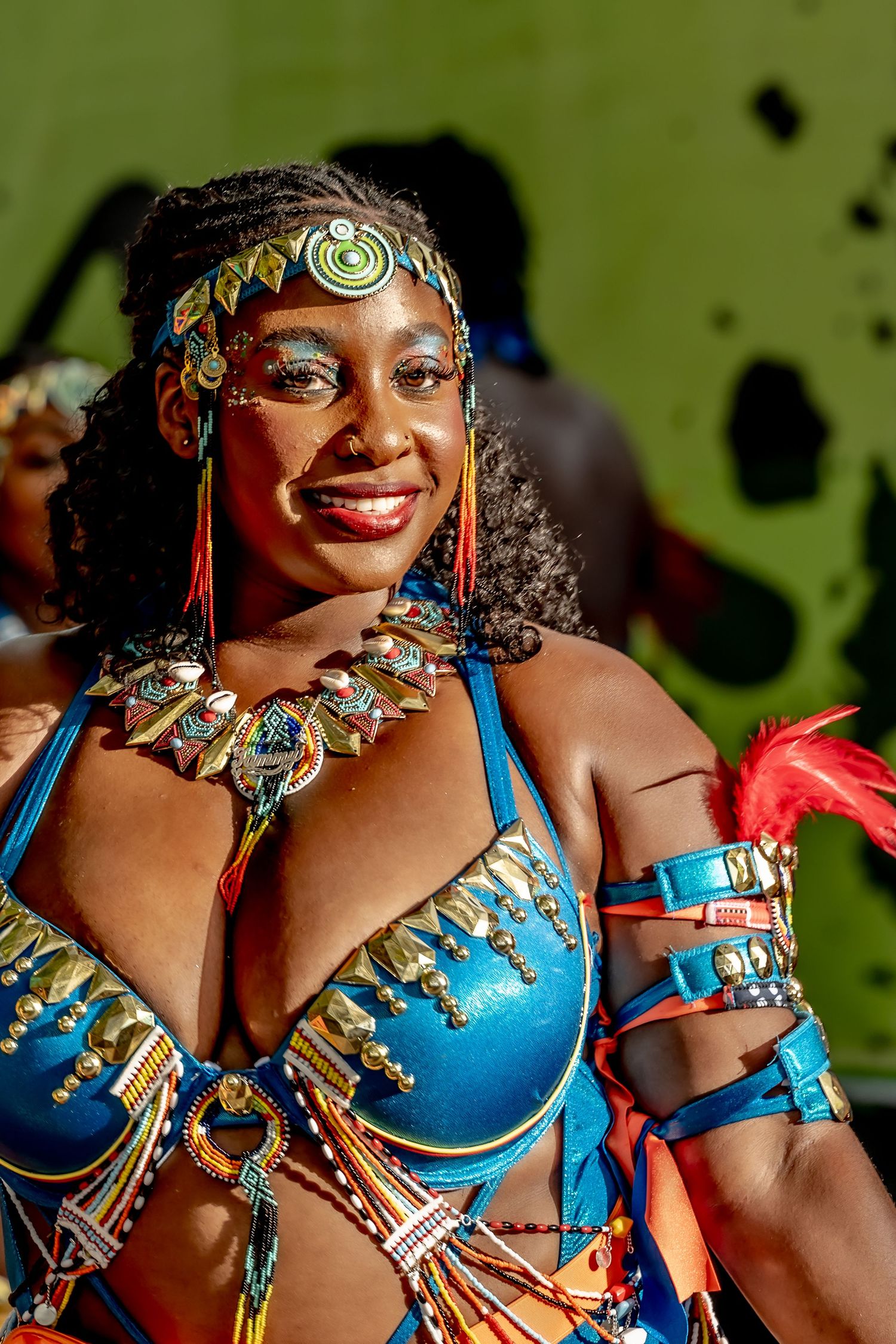 Smiling woman in vibrant blue carnival costume with gold accessories and colorful headpiece at a festive celebration.
