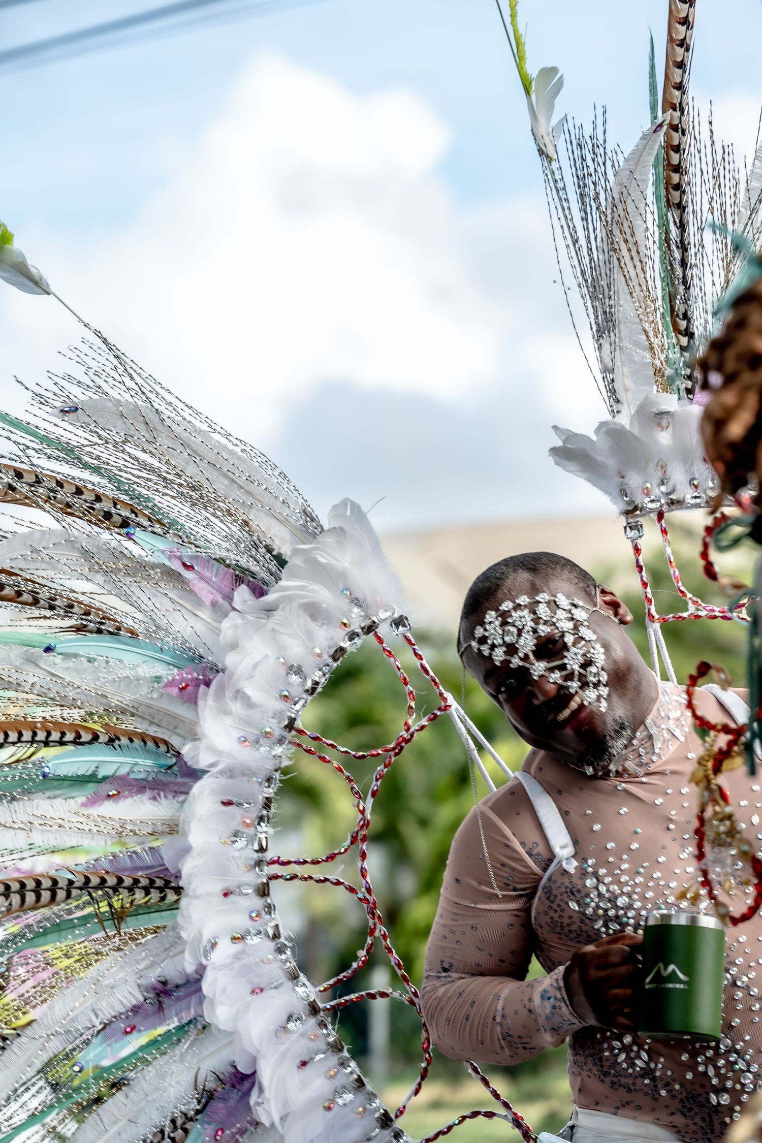 Carnival performer in elaborate white feathered headdress with pearl face decorations at a vibrant outdoor festival.