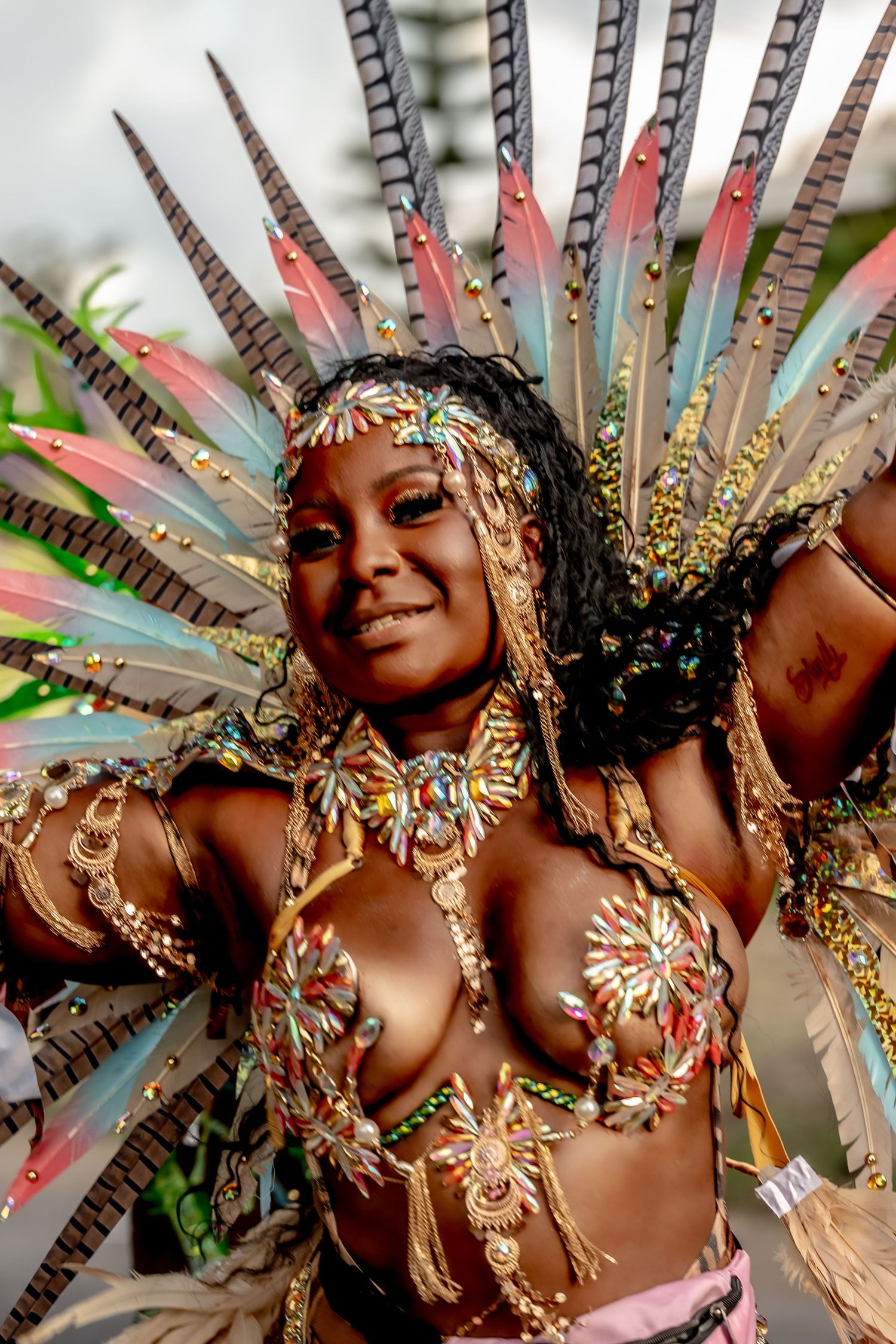 Woman in elaborate carnival costume with feathered headdress and ornate gold jeweled bikini top at festival.