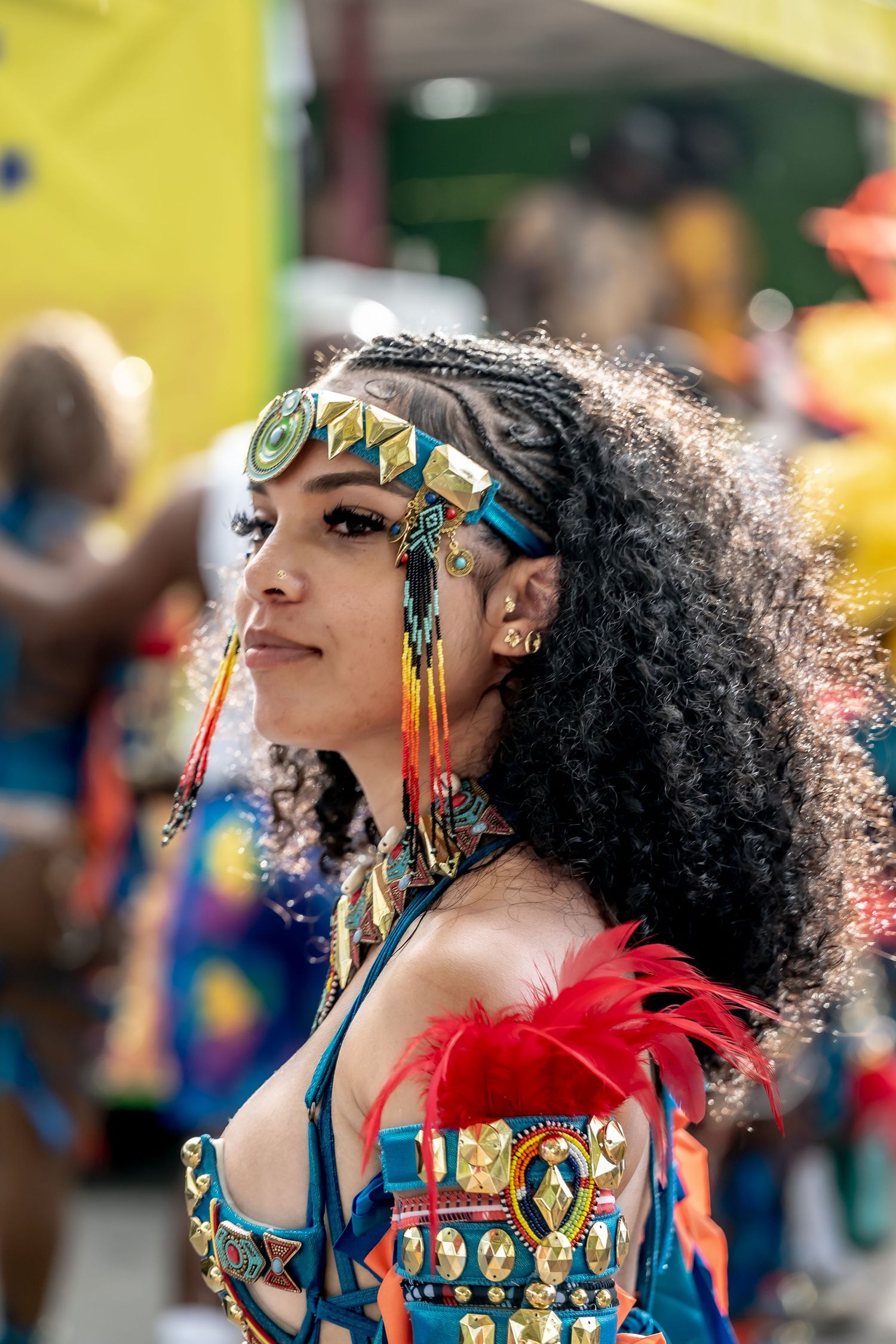 A woman in vibrant carnival costume with gold headpiece, colorful beads, and red feathers at a festive parade.