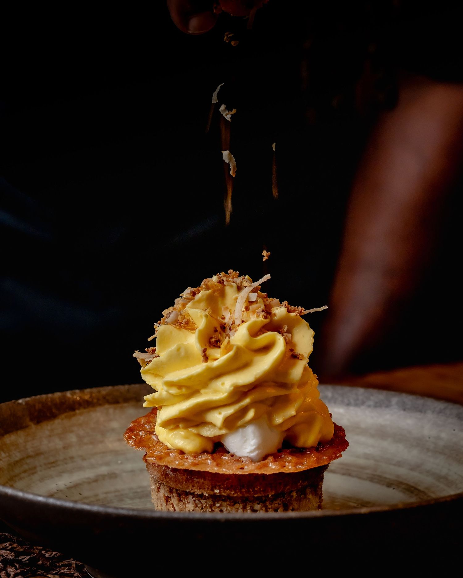 Elegant dessert tart topped with swirled golden cream and toasted coconut flakes on a rustic ceramic plate.