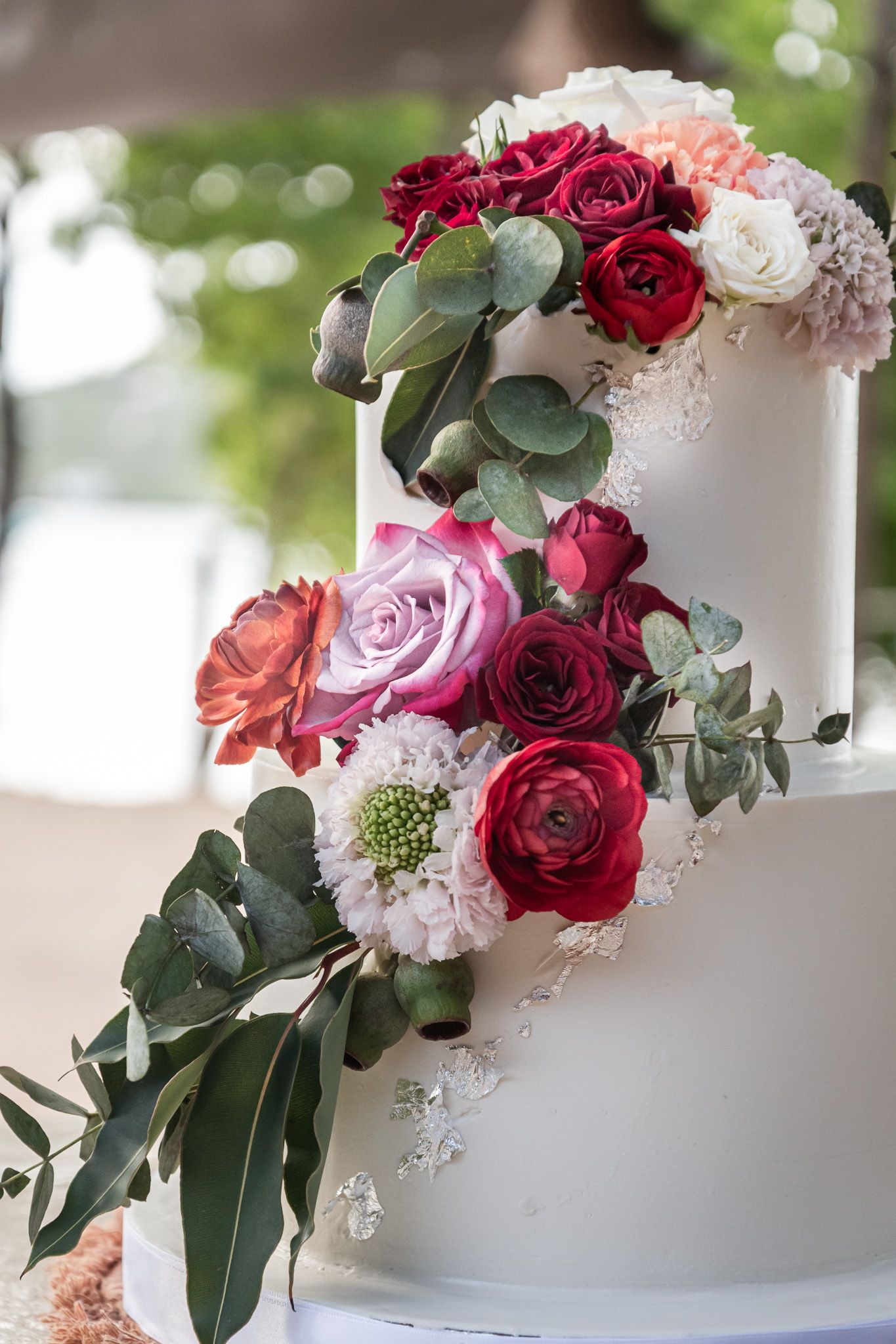Elegant white wedding cake decorated with cascading burgundy and pink roses with eucalyptus greenery.
