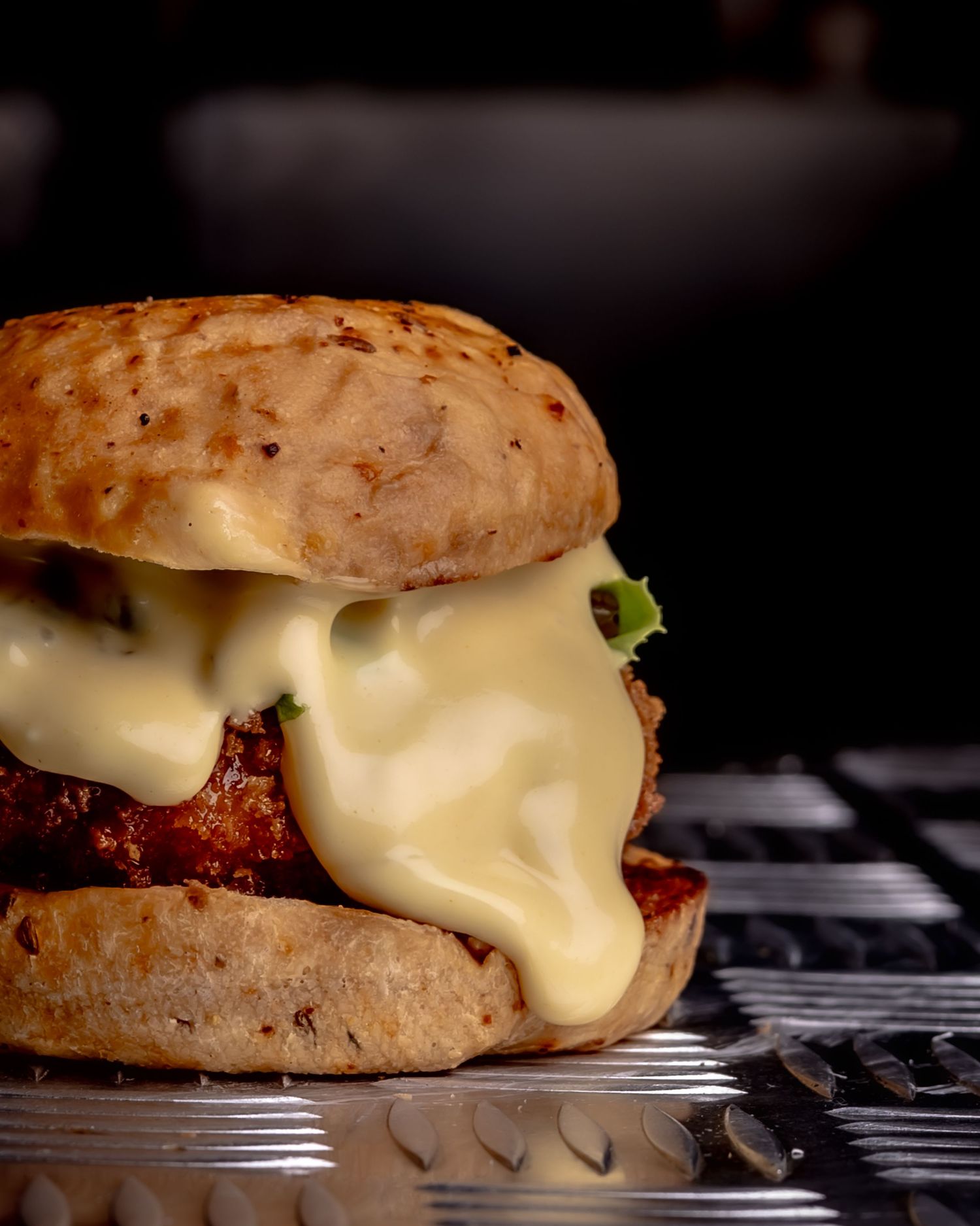 Close-up of a juicy burger topped with melted cheese on a toasted bun, served on a metal tray.