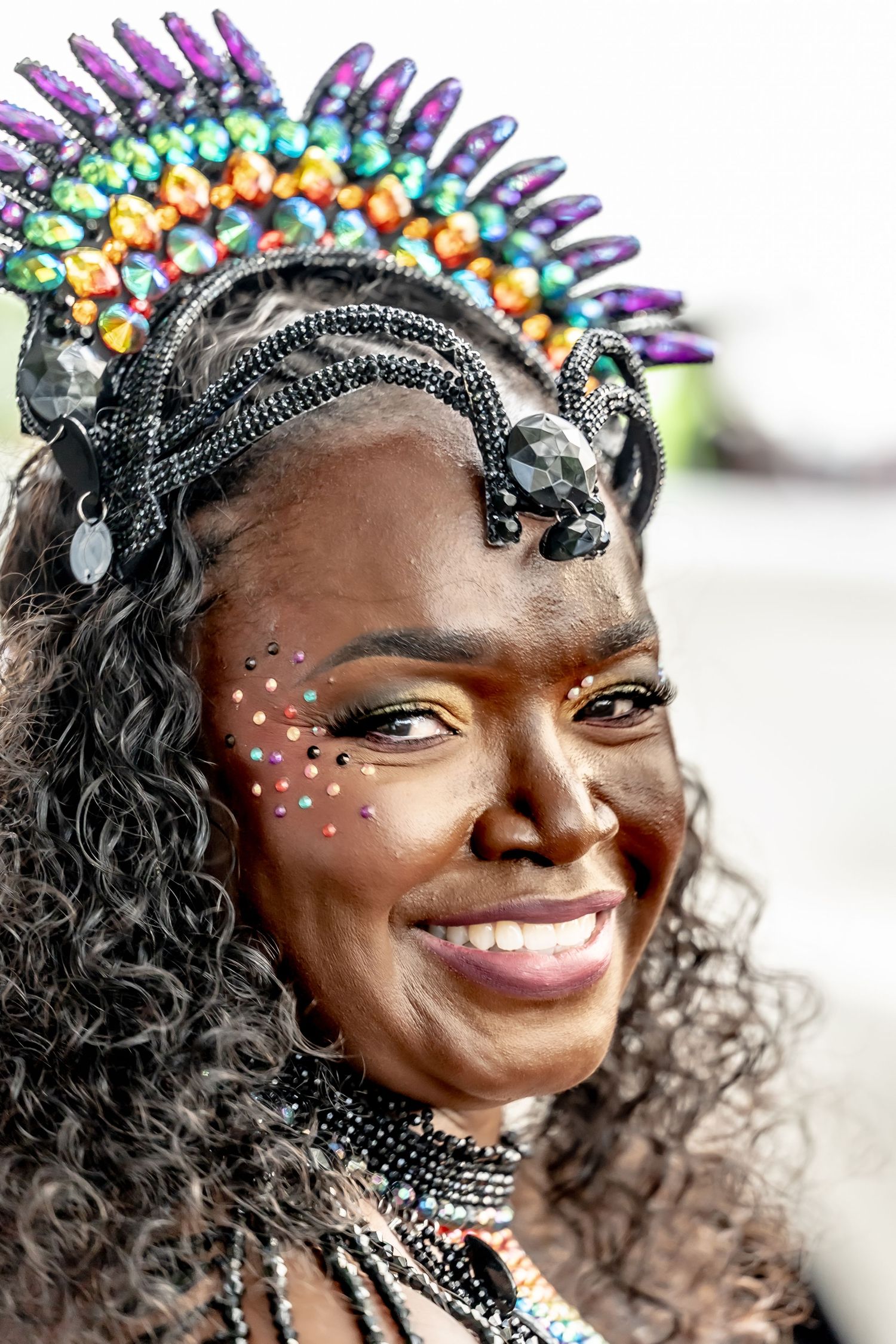 Smiling woman in colorful beaded crown and festival face gems at carnival celebration.
