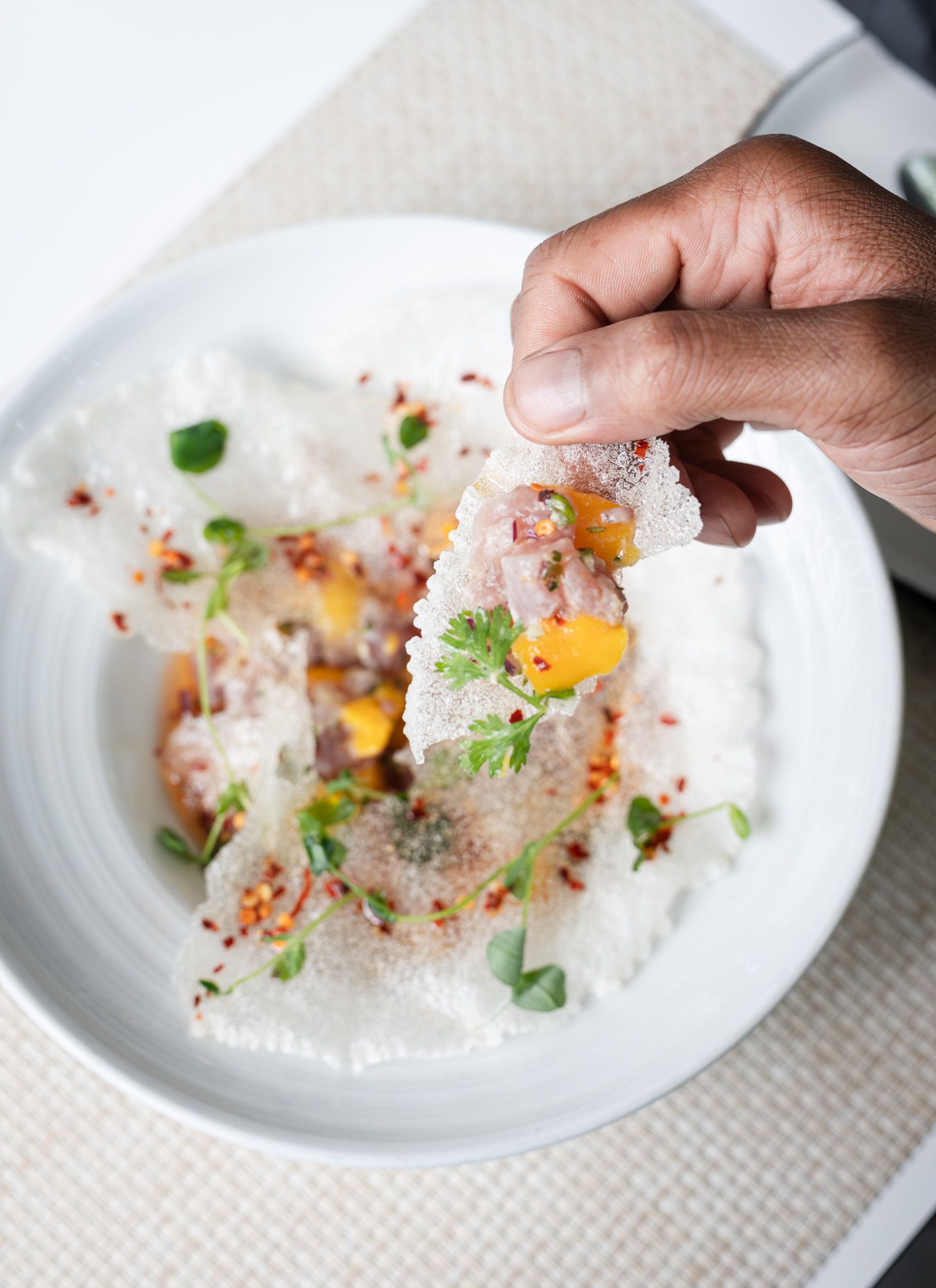 Hands drizzling olive oil over a plated dish with egg yolk, shaved cheese, and fresh herbs.