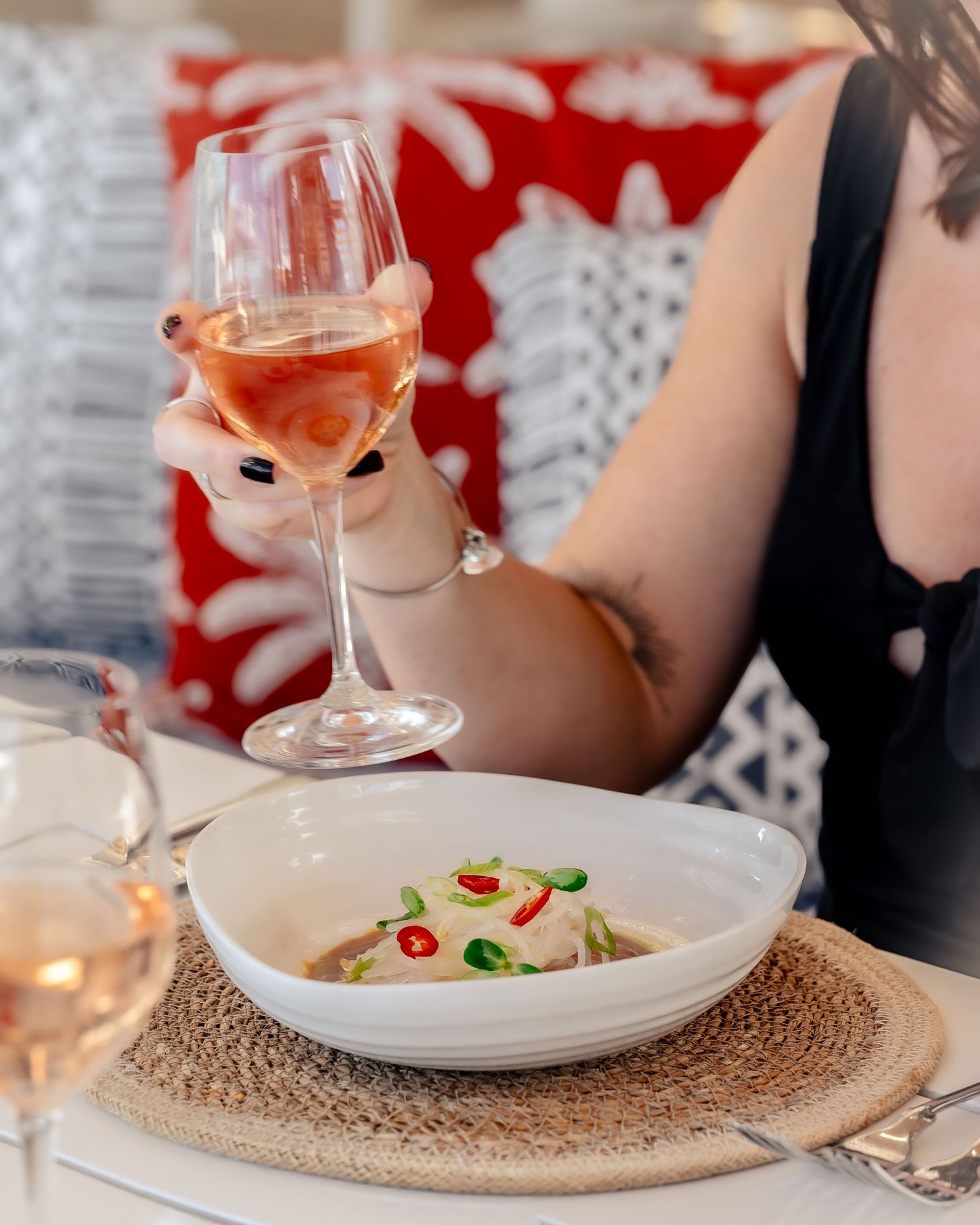 Woman holding rosé wine glass over a white bowl of seafood dish at an elegant restaurant table.