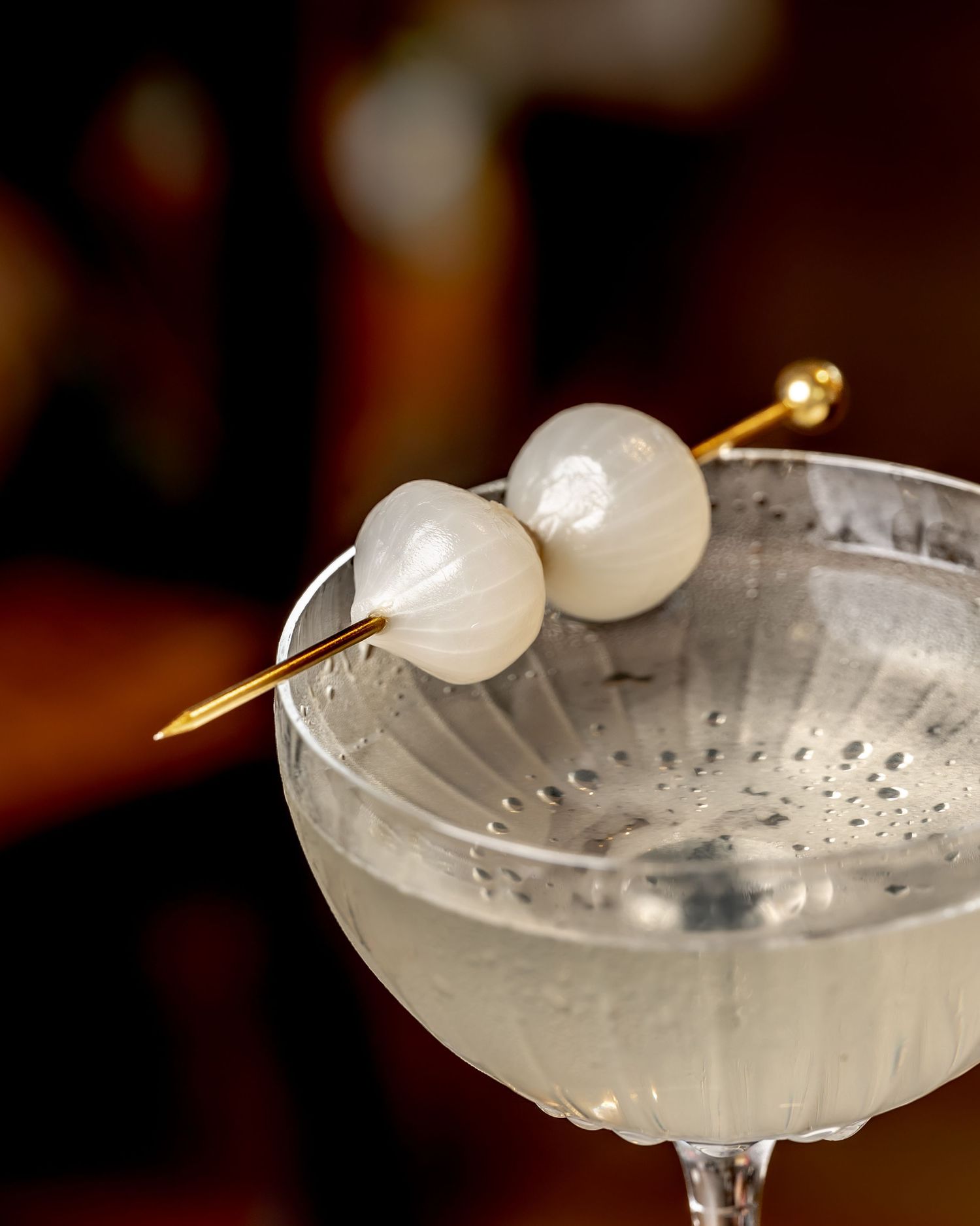A classic Gibson martini in a coupe glass garnished with two pearl onions on a gold cocktail pick.