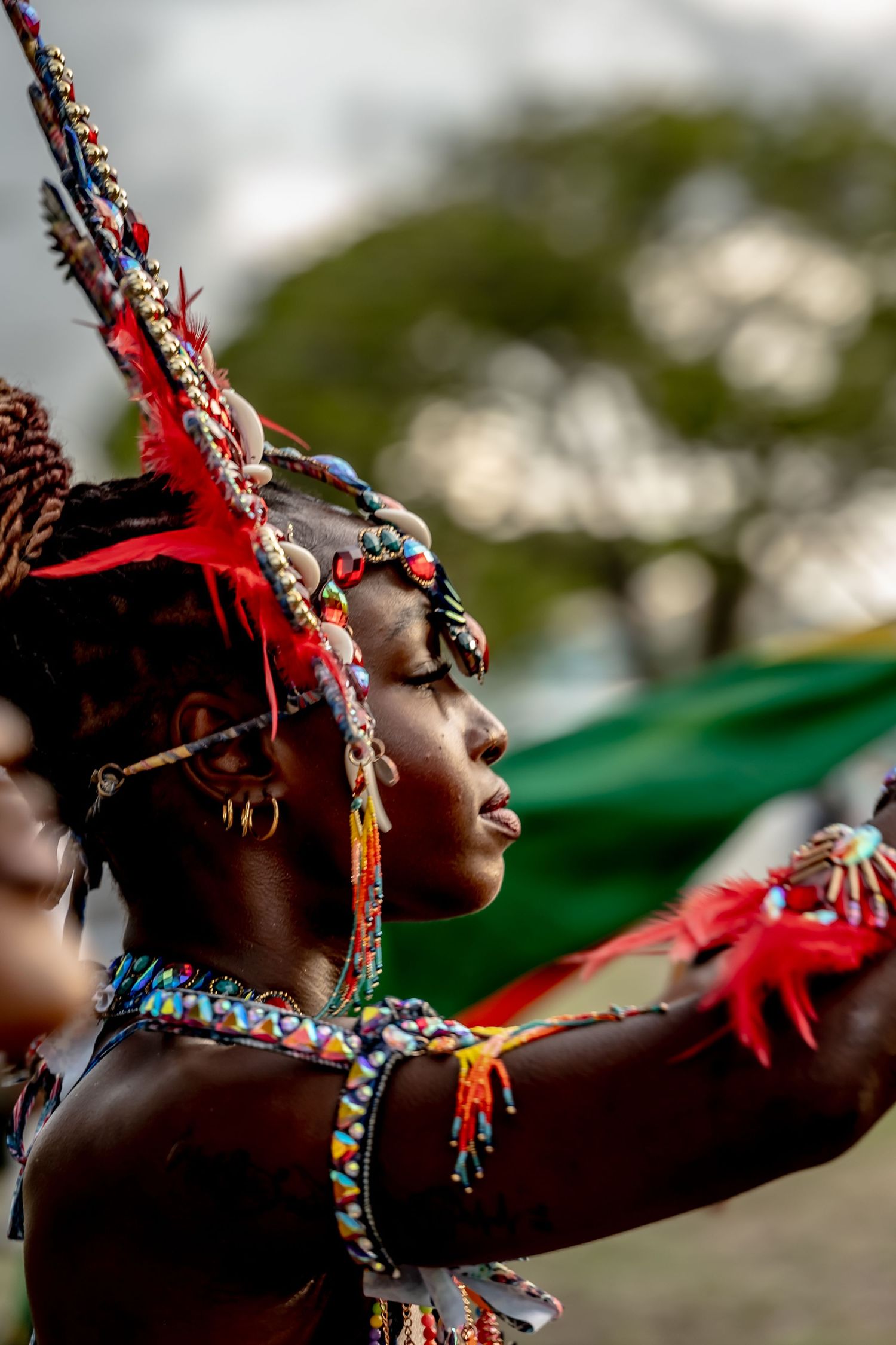 African woman in colorful beaded costume with feathers and headdress performing traditional cultural dance outdoors.
