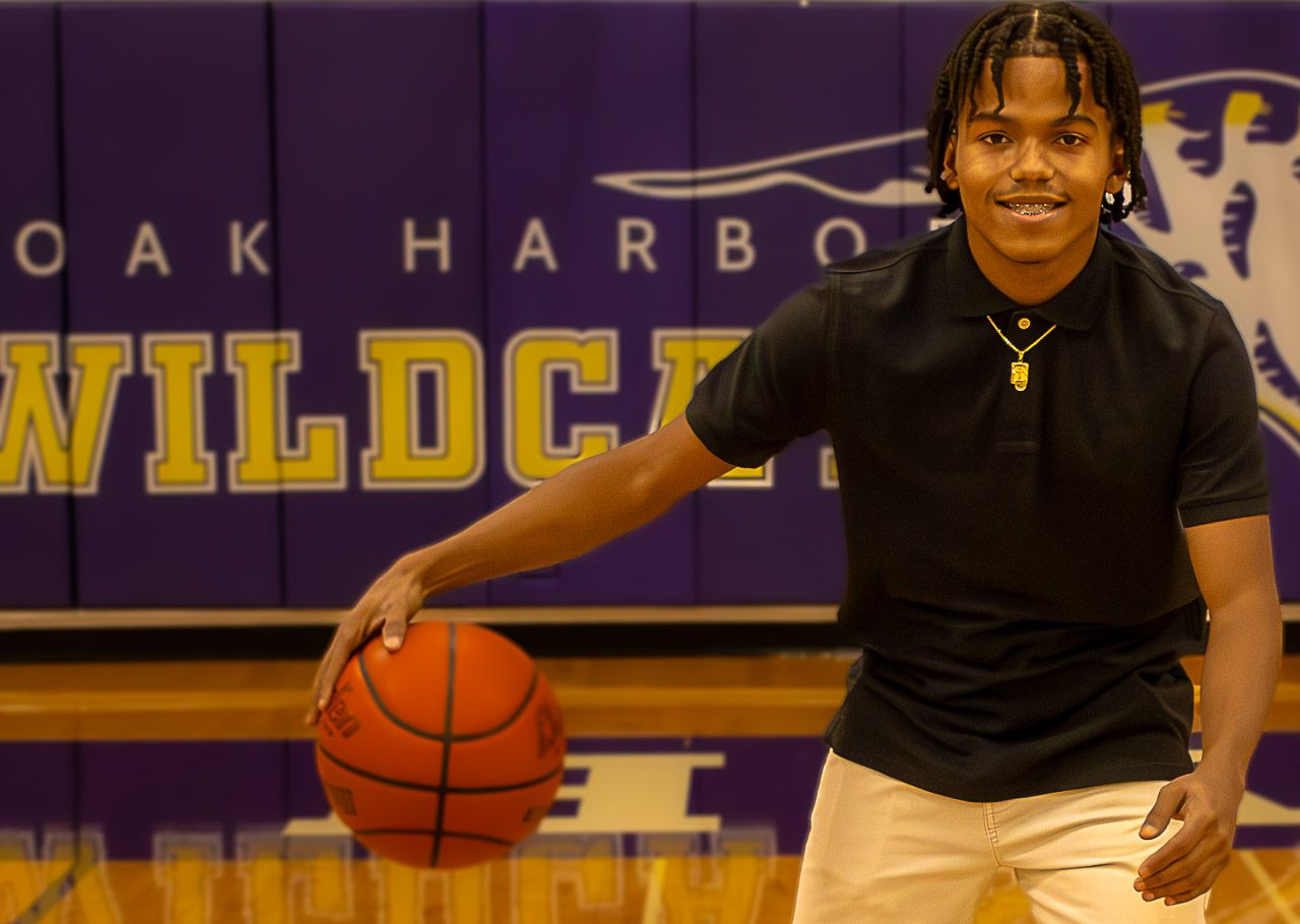 Young athlete poses with basketball in front of Oak Harbor Wildcats gym backdrop. Senior picture