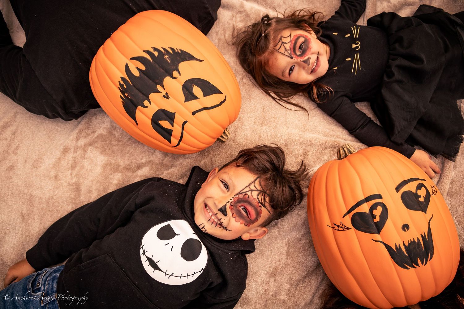 Two children with Halloween face paint pose with carved jack-o-lantern pumpkins in a festive fall photo. Fall Mini.