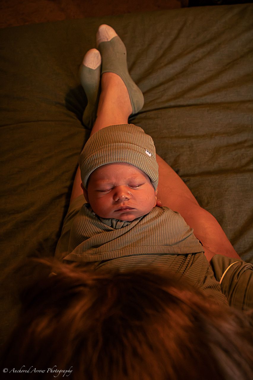 Sleeping newborn baby wrapped in green swaddle wearing knit hat resting on chest.