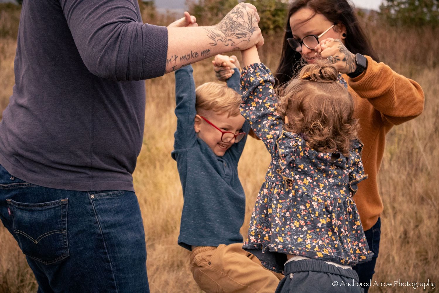 Family of four playfully swinging two young children in an autumn field during a fun outdoor photo session.