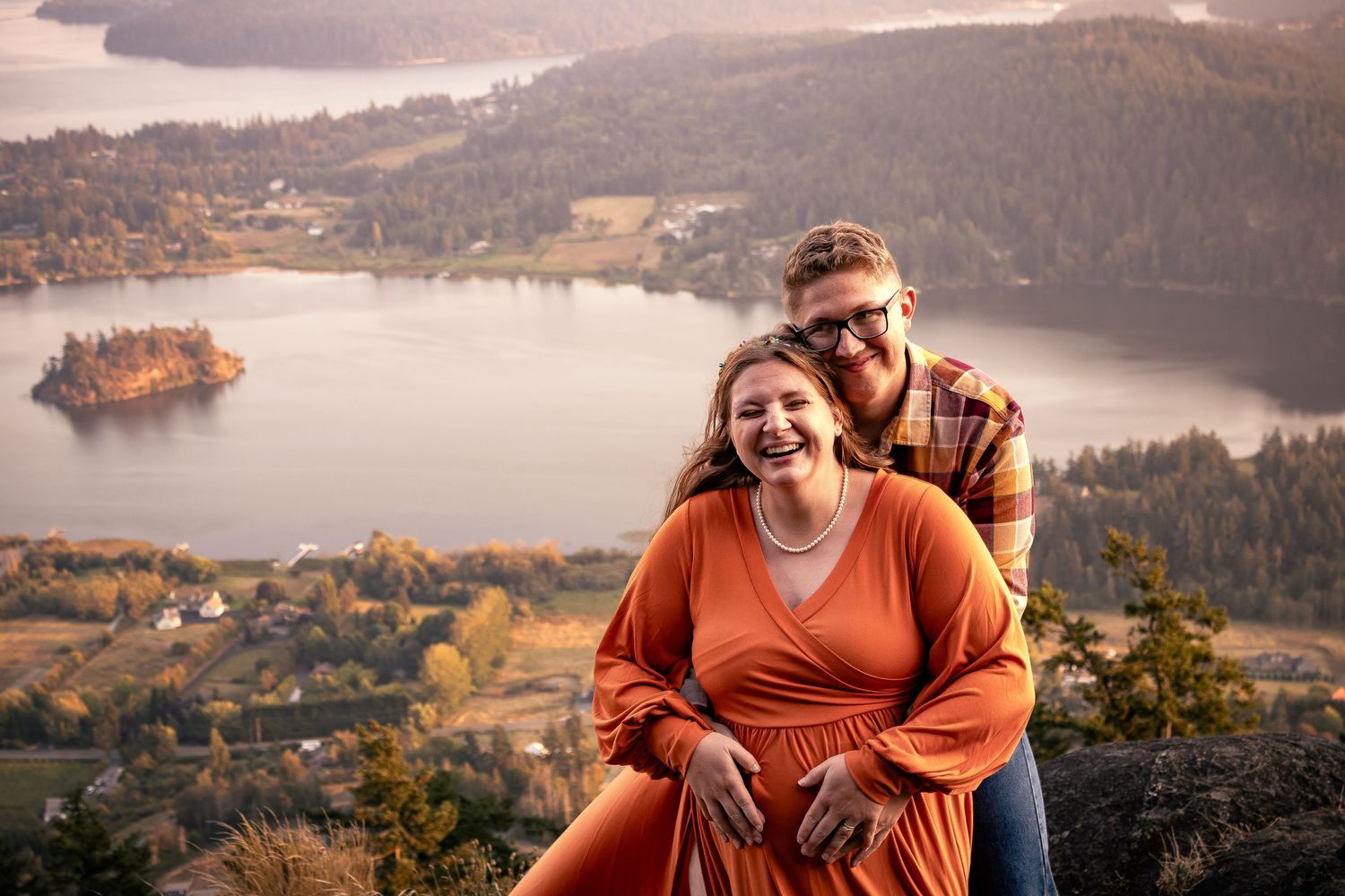 Happy couple laughing together on a mountain overlook with a scenic lake and autumn forest below.