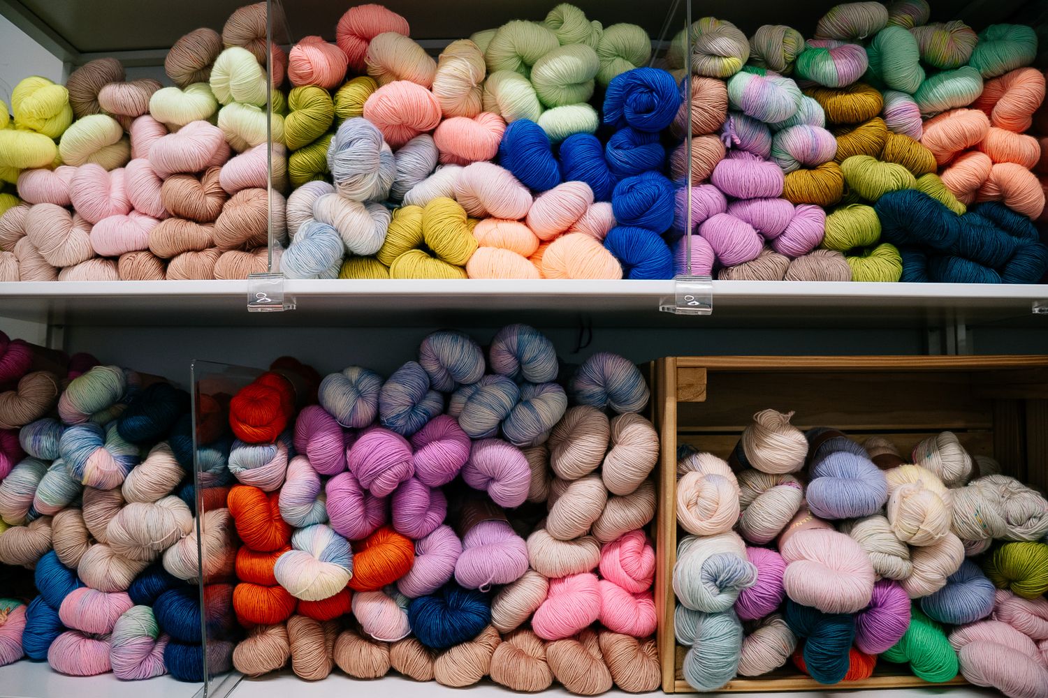 Colorful yarn skeins arranged on shelves in pastel and vibrant hues, perfect for knitting and crocheting projects.
