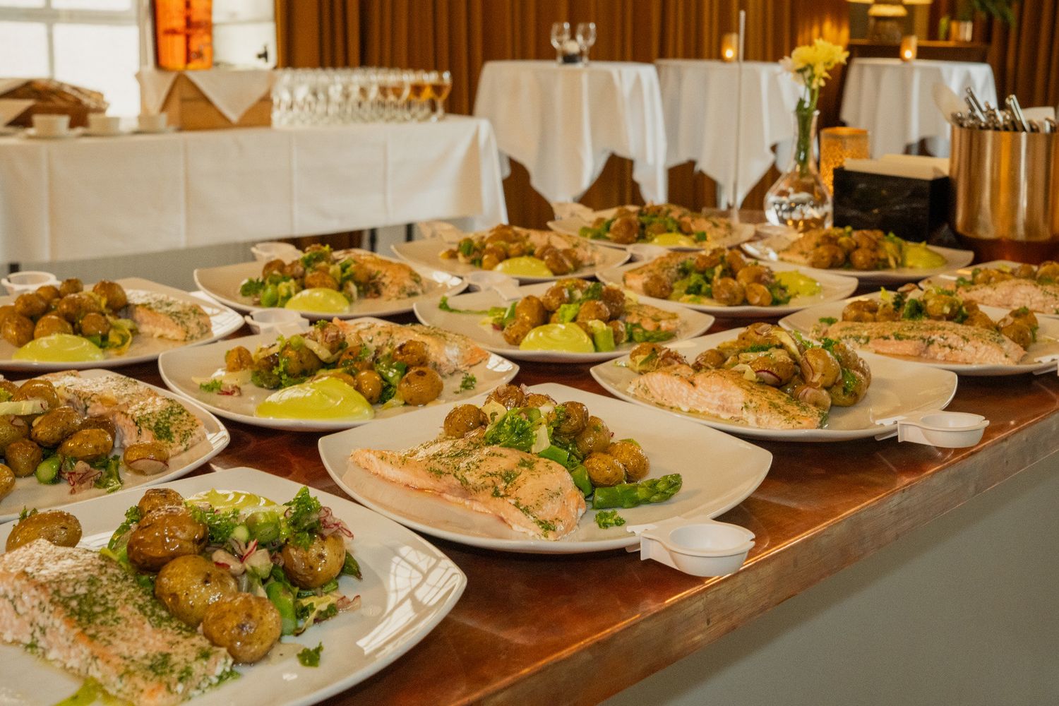 Rows of plated salmon dishes with roasted potatoes served at a formal catered event.