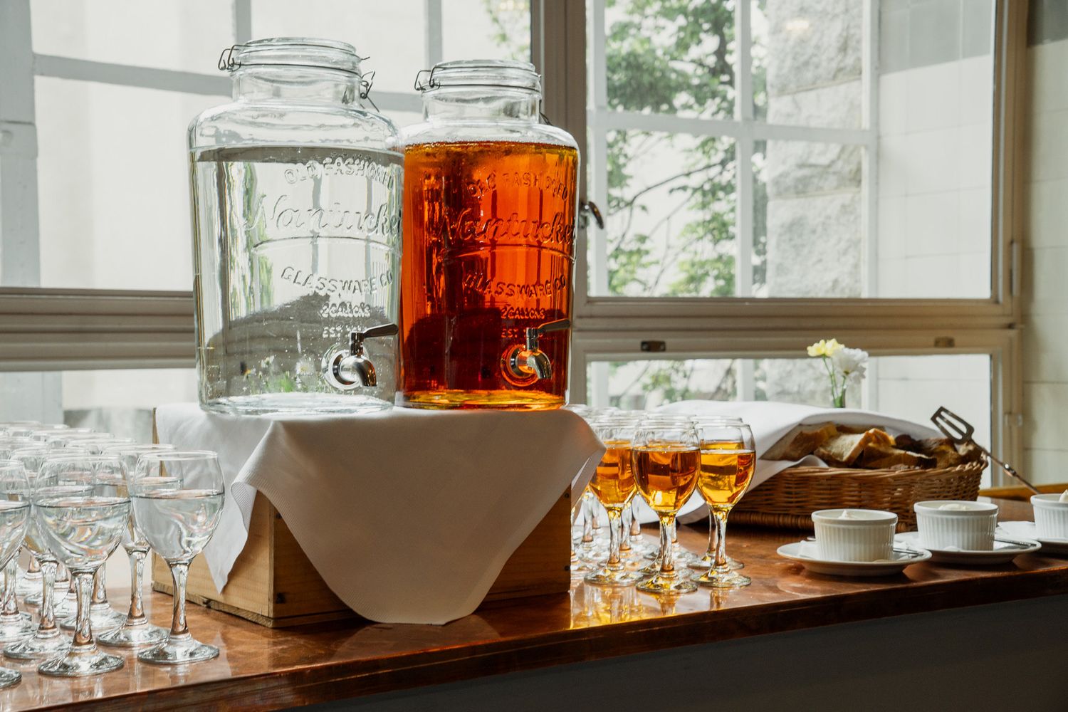 Glass beverage dispensers with amber drinks and crystal glasses on a wooden buffet table.