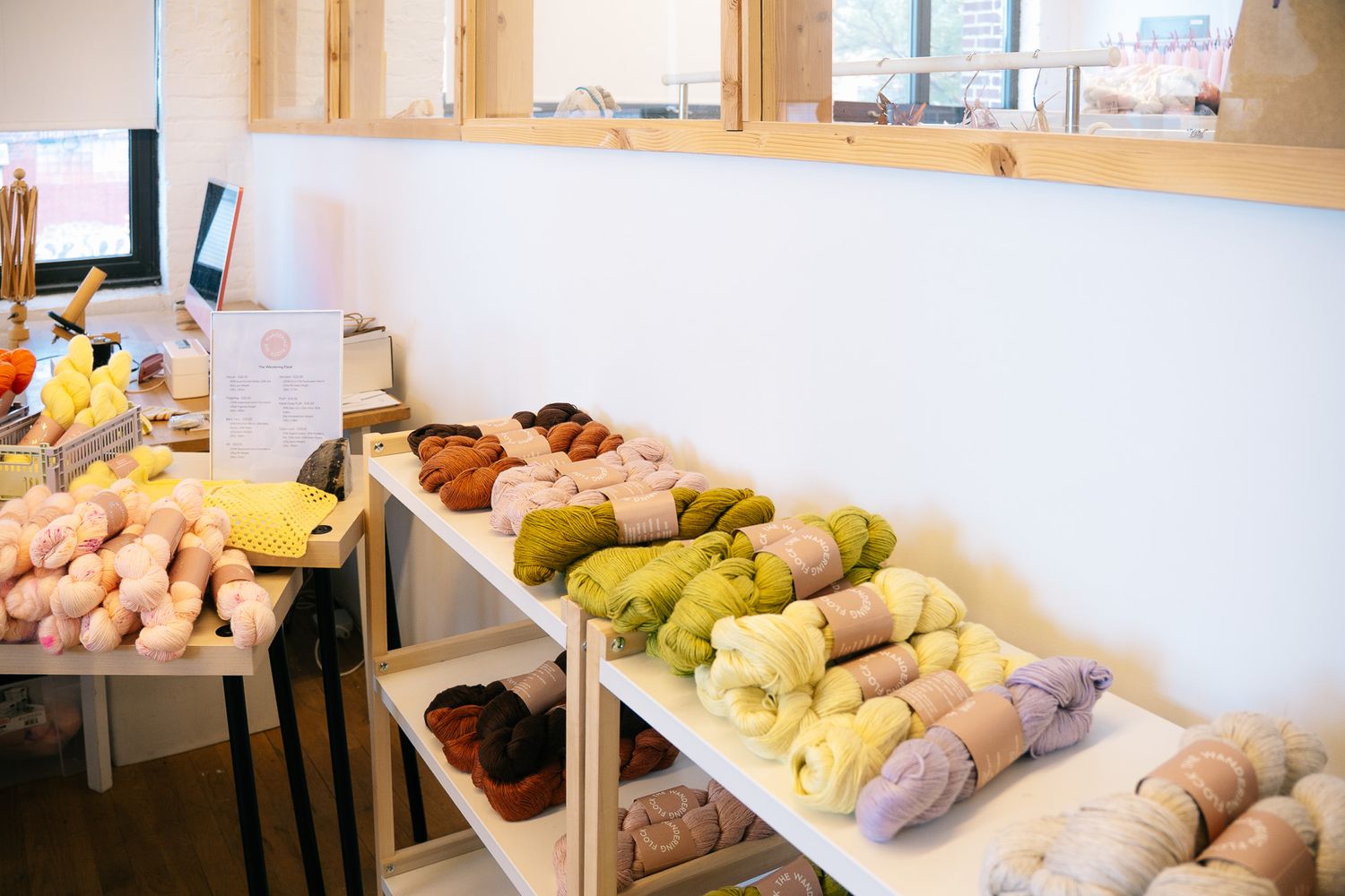 Colorful skeins of yarn displayed on white shelves in a cozy yarn shop with natural wood accents and bright windows.