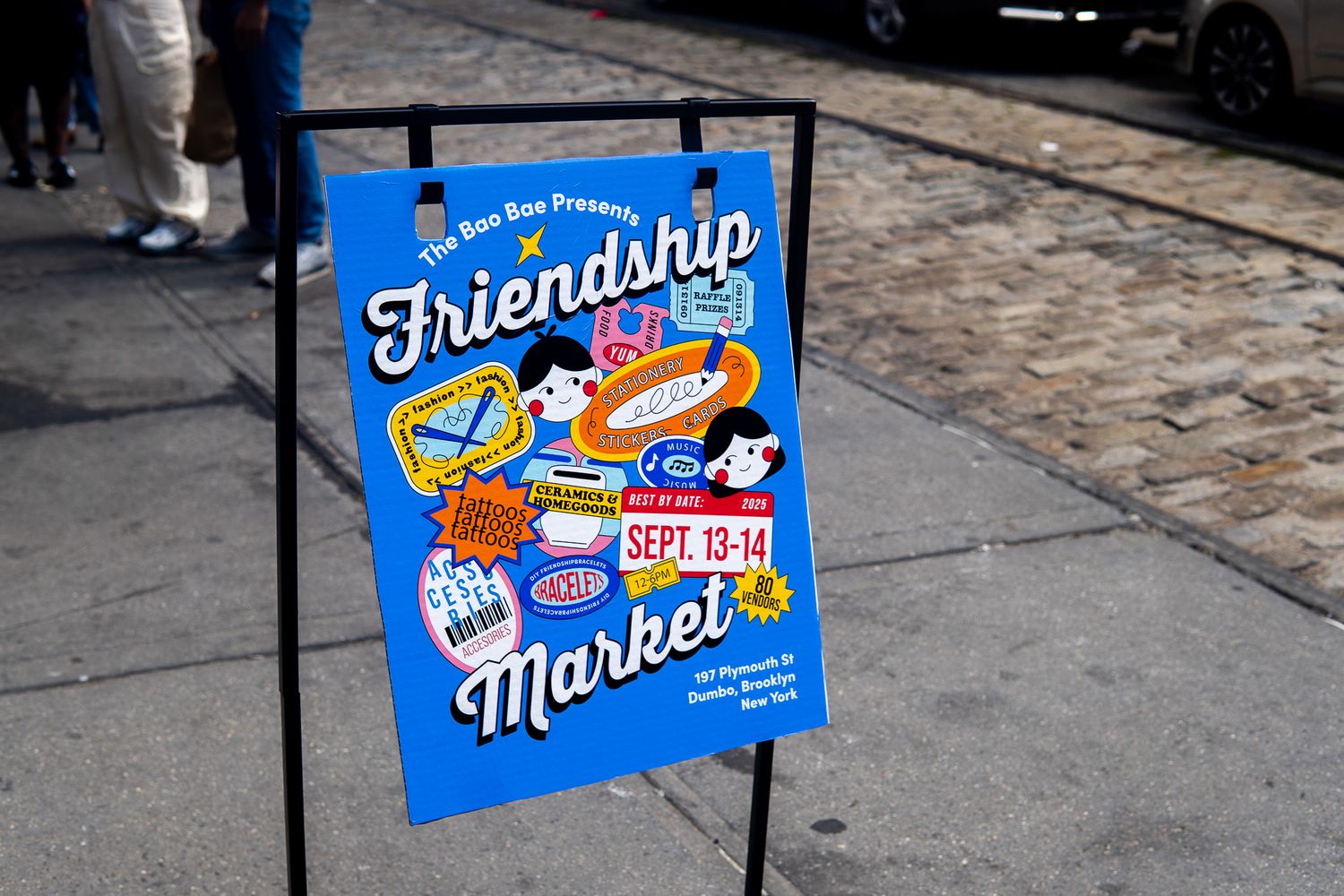 Blue poster for Friendship Market event;\ Sept 13-14, displayed on sidewalk easel.