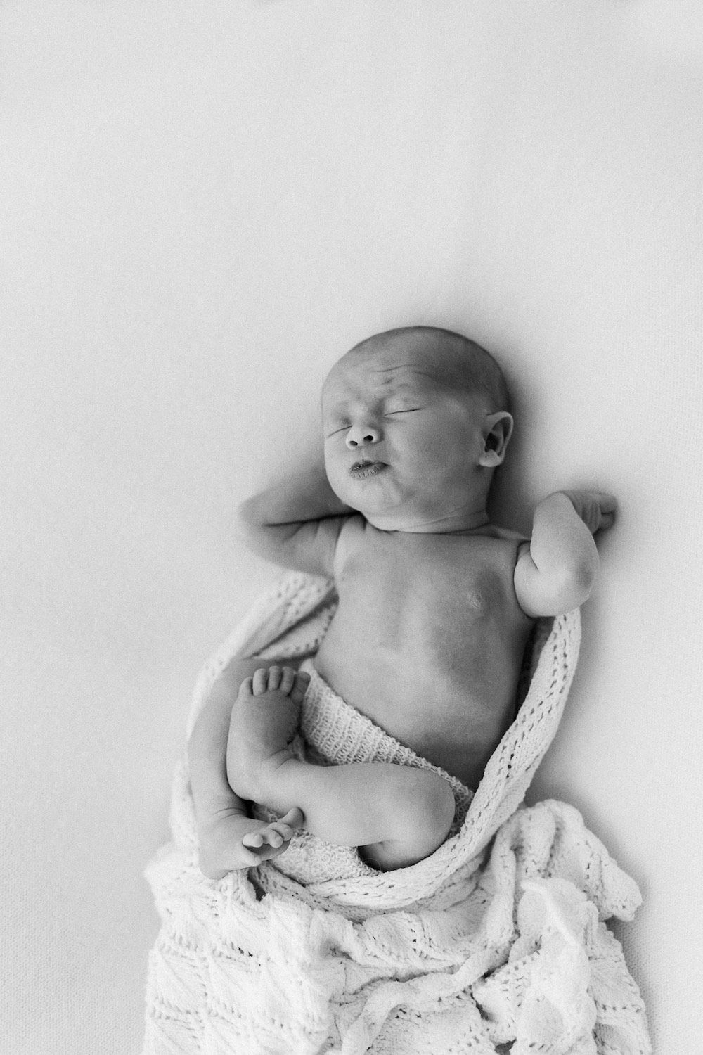 Black and white portrait of sleeping newborn baby loosely wrapped in knit blanket. Affordable newborn photography.