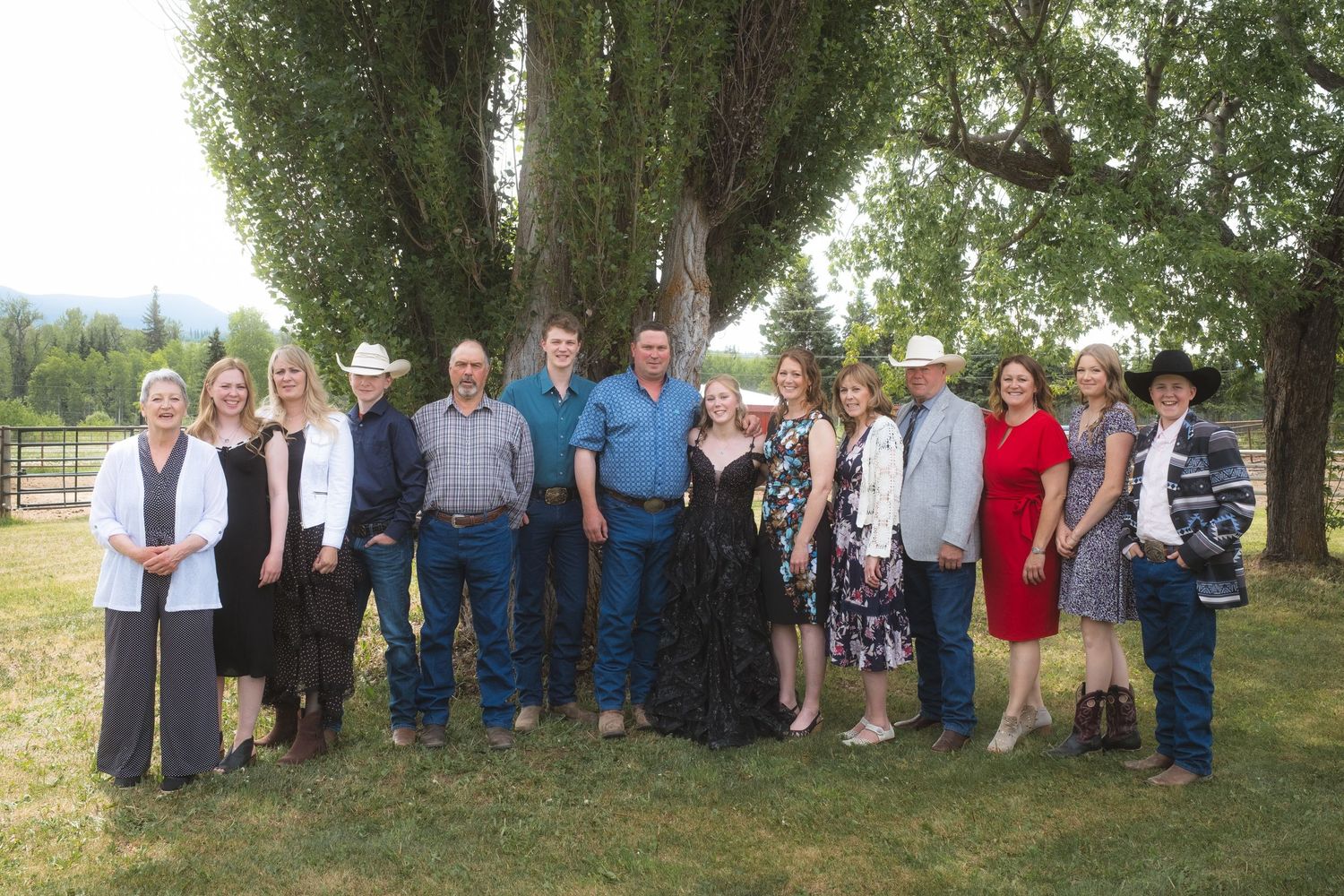 Large family group portrait outdoors on a ranch with willow tree backdrop, mix of formal and western attire.